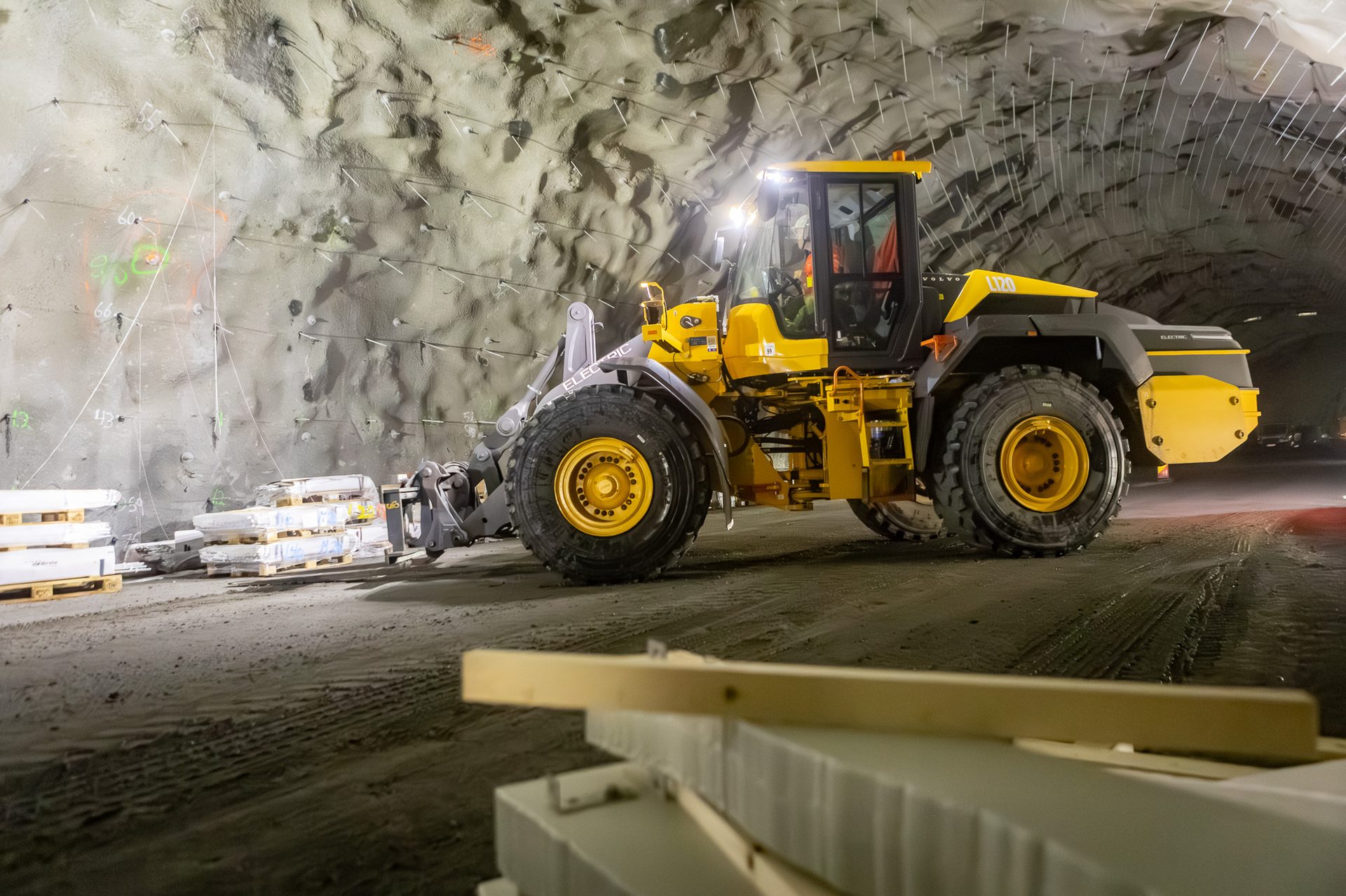 Yellow electric Volvo wheel loader in a reinforced tunnel with construction materials.