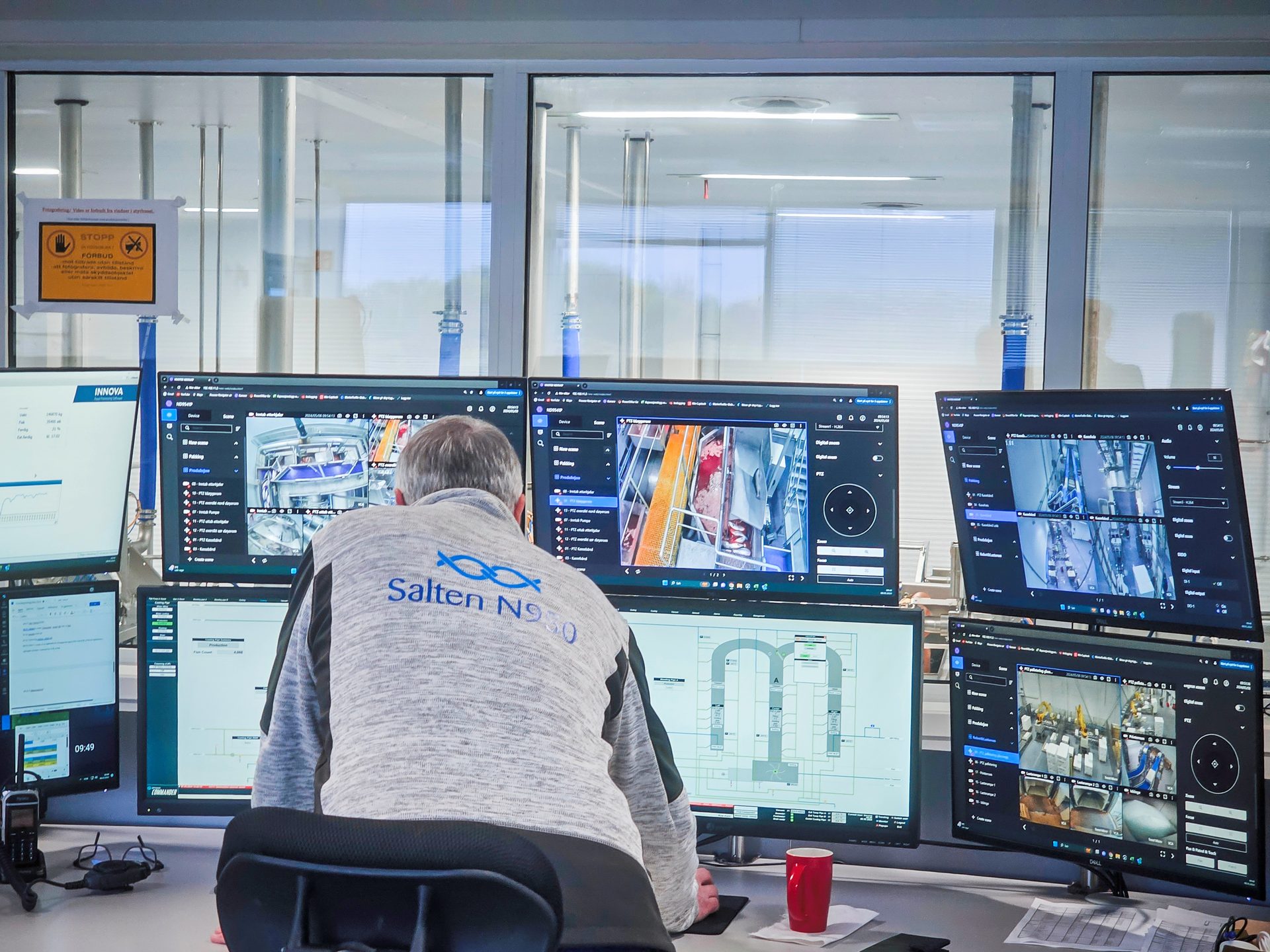 Man in a control room monitors multiple screens displaying industrial processes and surveillance footage.