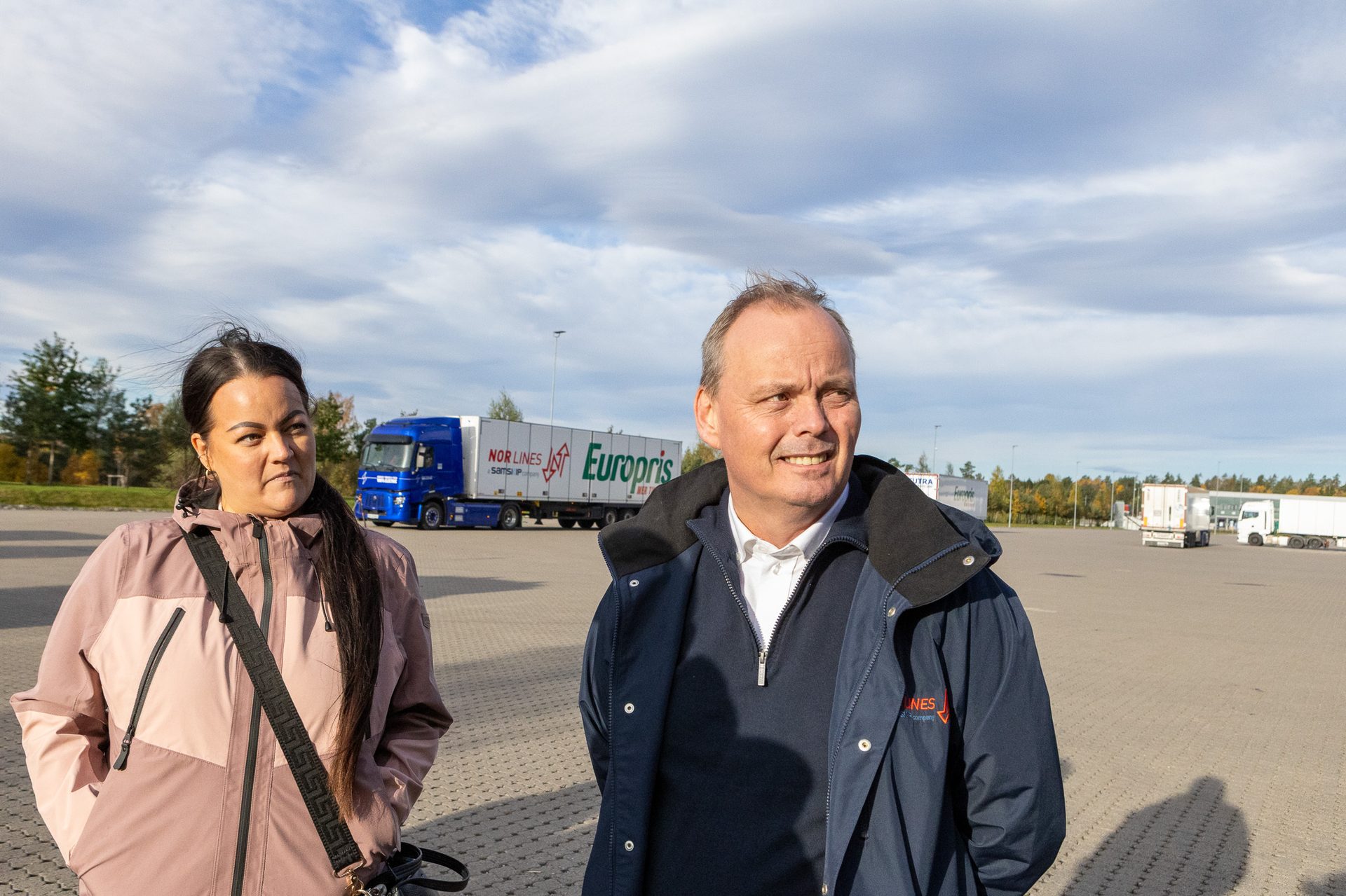 A man and a woman in a parking lot, a blue "Europris" truck behind them.