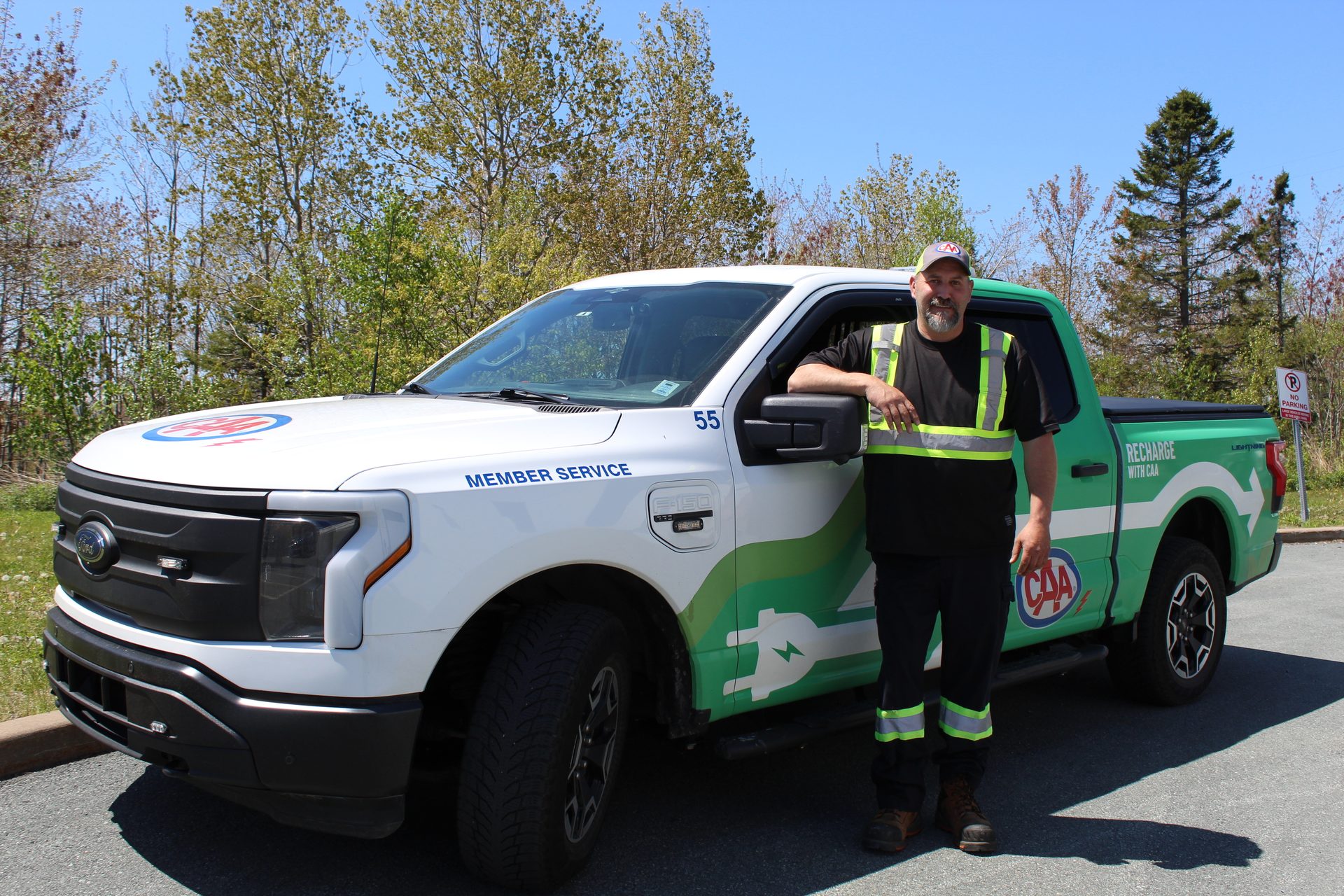 Man in high-vis vest stands next to a white and green CAA electric service truck.