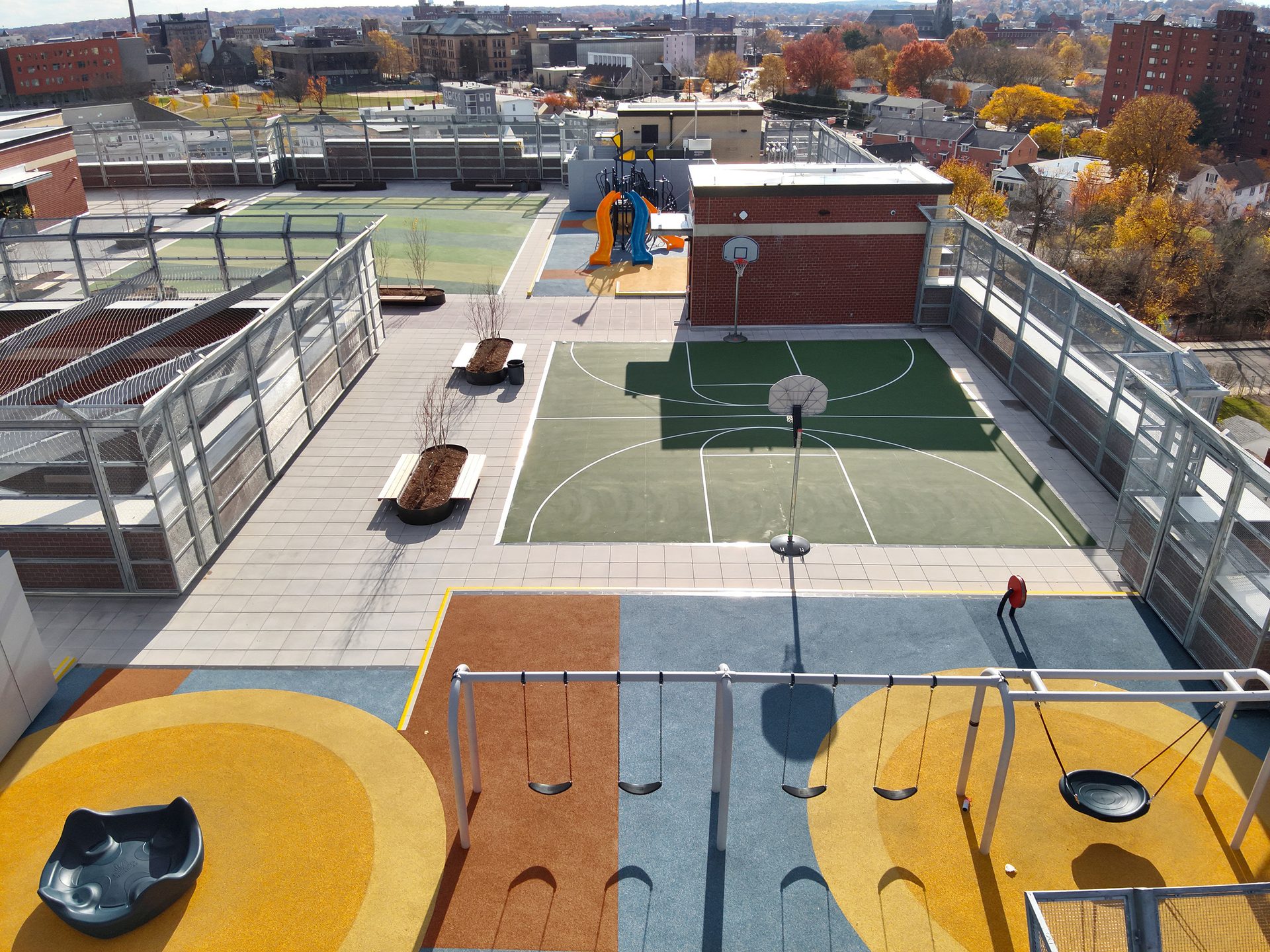 Rooftop recreation area: playground, basketball court, multi-sport court, and cityscape in autumn.