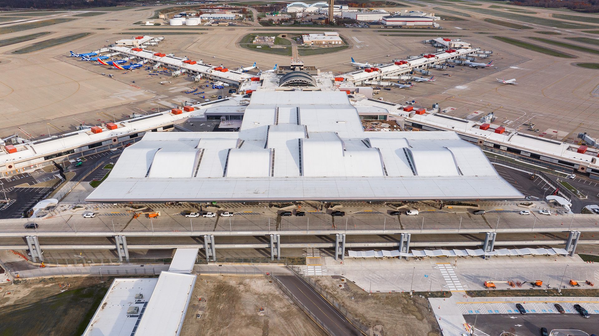 Aerial view of a large, modern airport terminal complex with numerous aircraft parked at boarding gates.