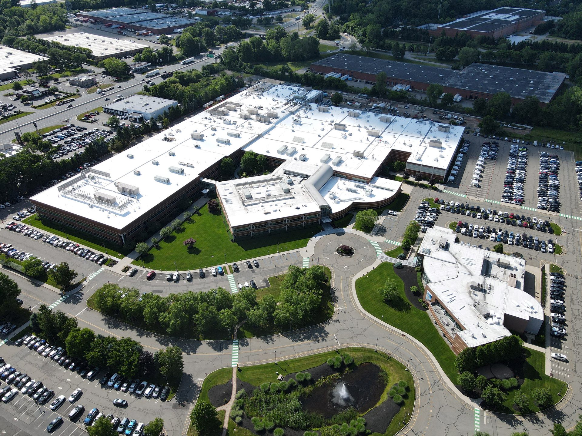 Aerial view of a large corporate campus with multiple white-roofed buildings, extensive parking, roads, and green spaces.