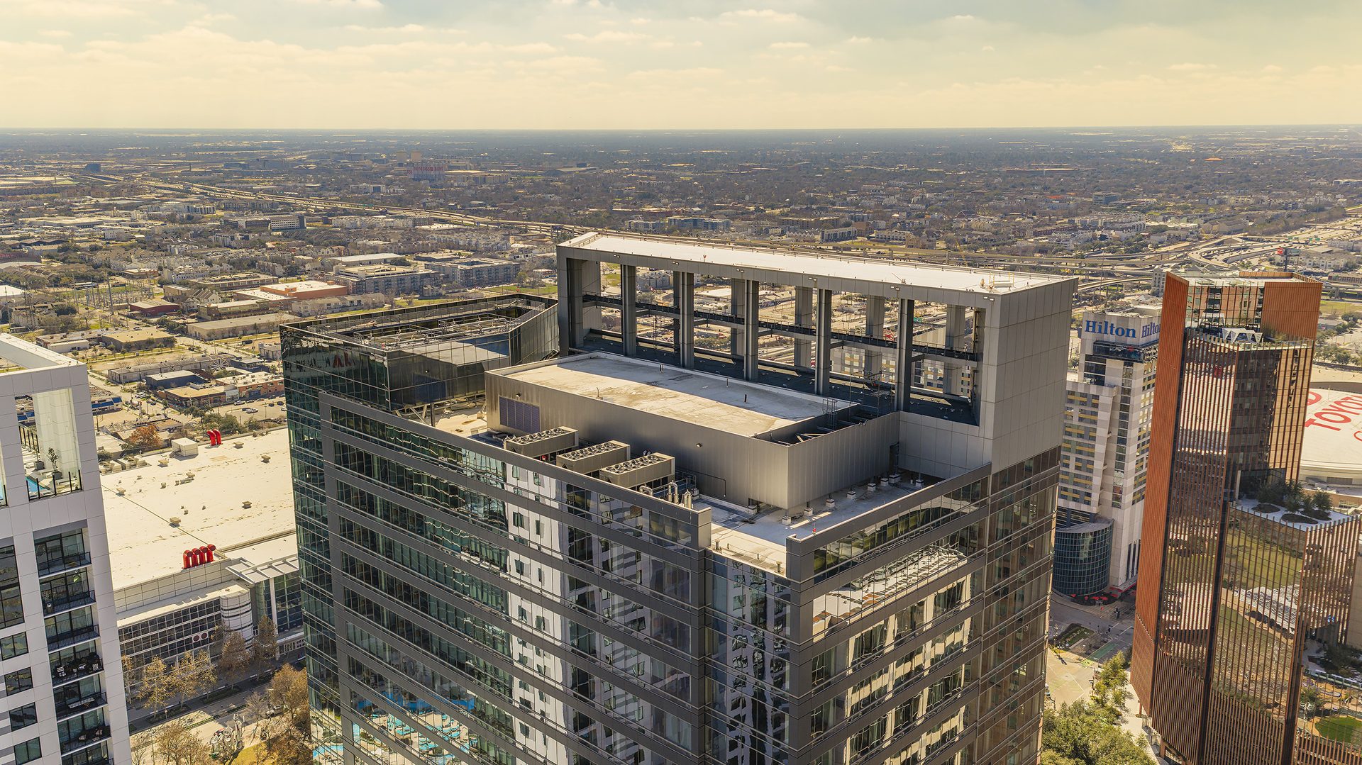Aerial view of a modern urban landscape featuring a dark glass high-rise building and other towers.