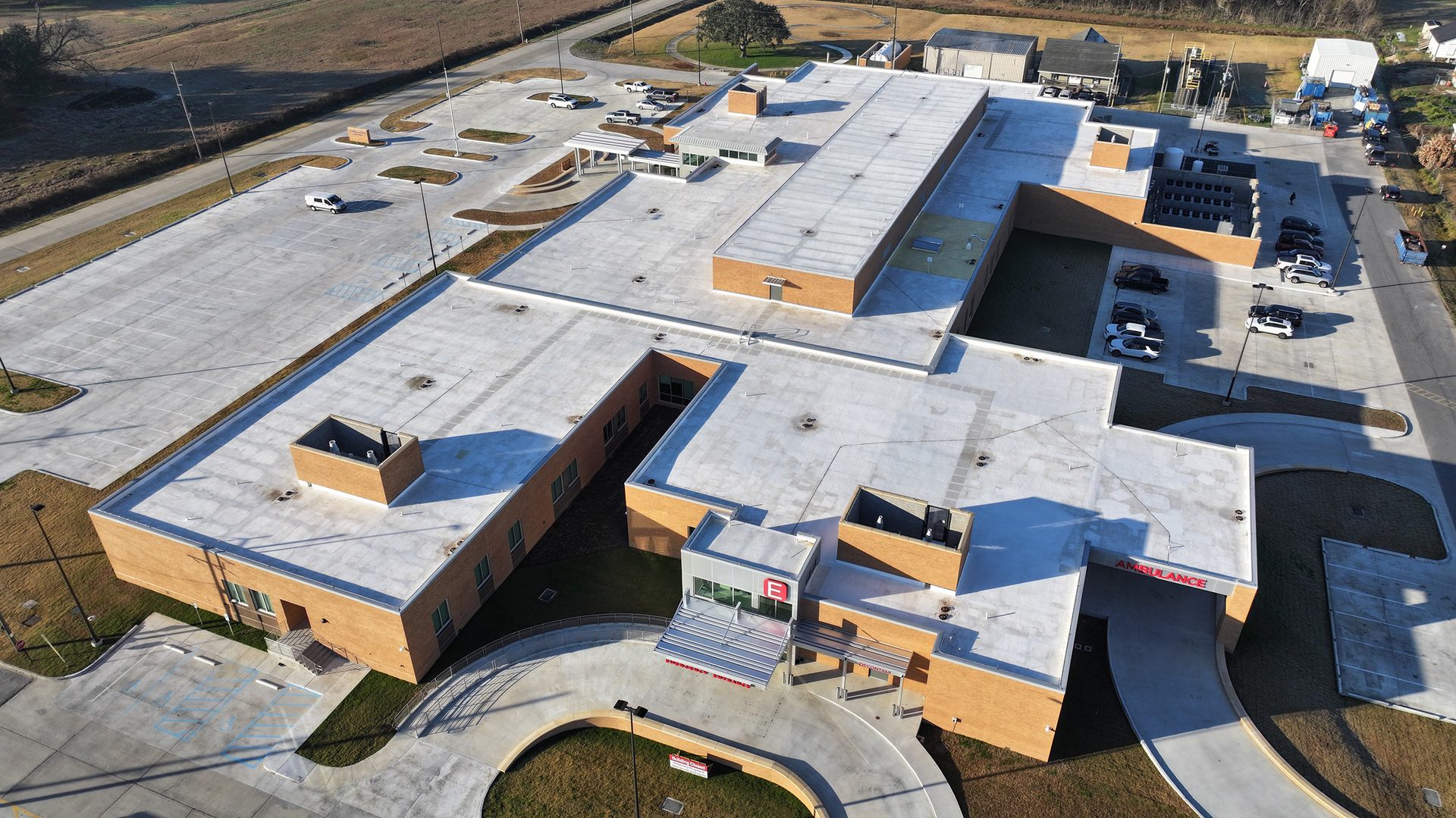 Aerial view of a modern brick medical facility with flat roofs, multiple parking lots, and ambulance entrance.