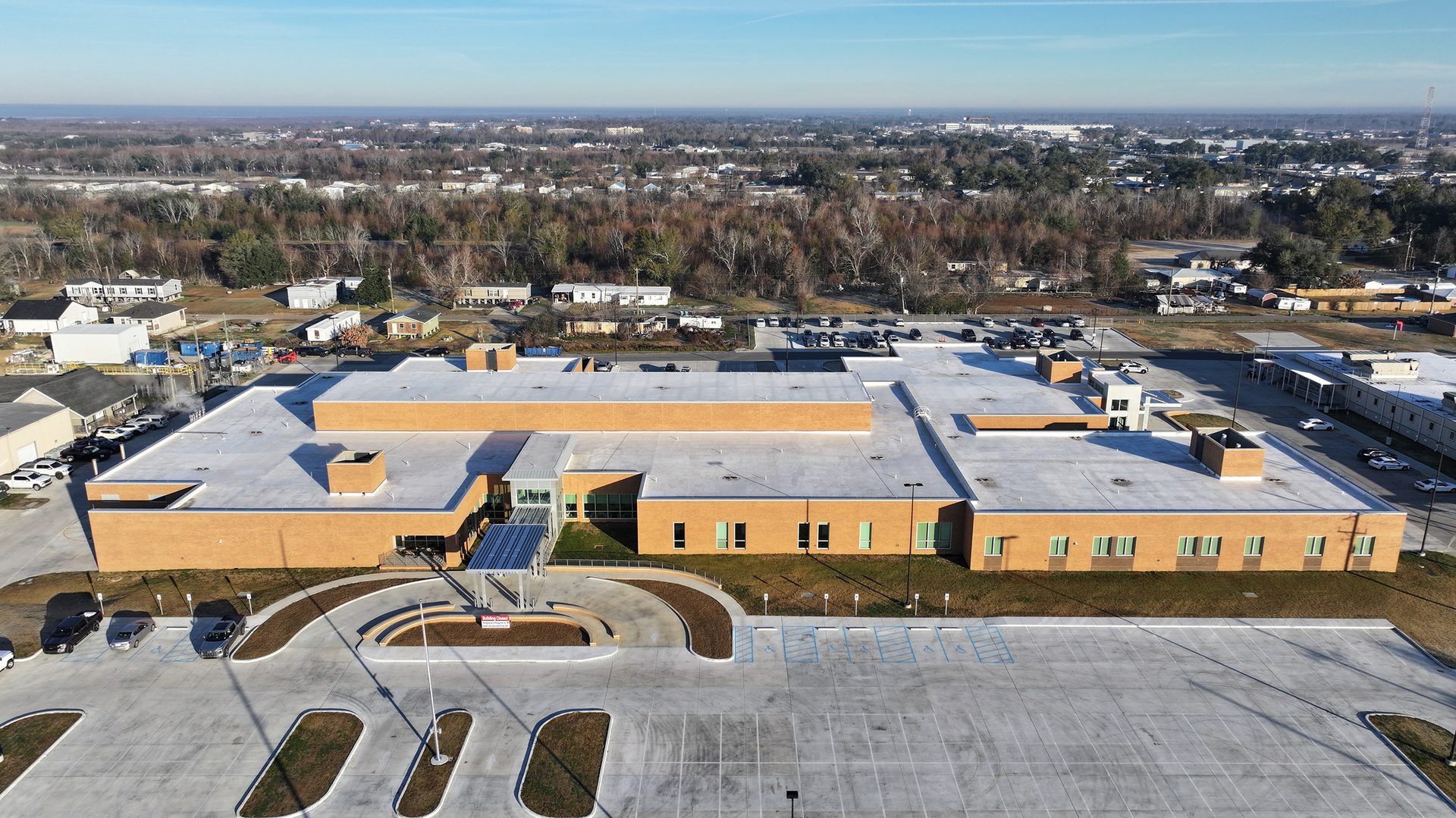 Aerial view of a large, modern, light brown brick building with a white roof and extensive parking areas.