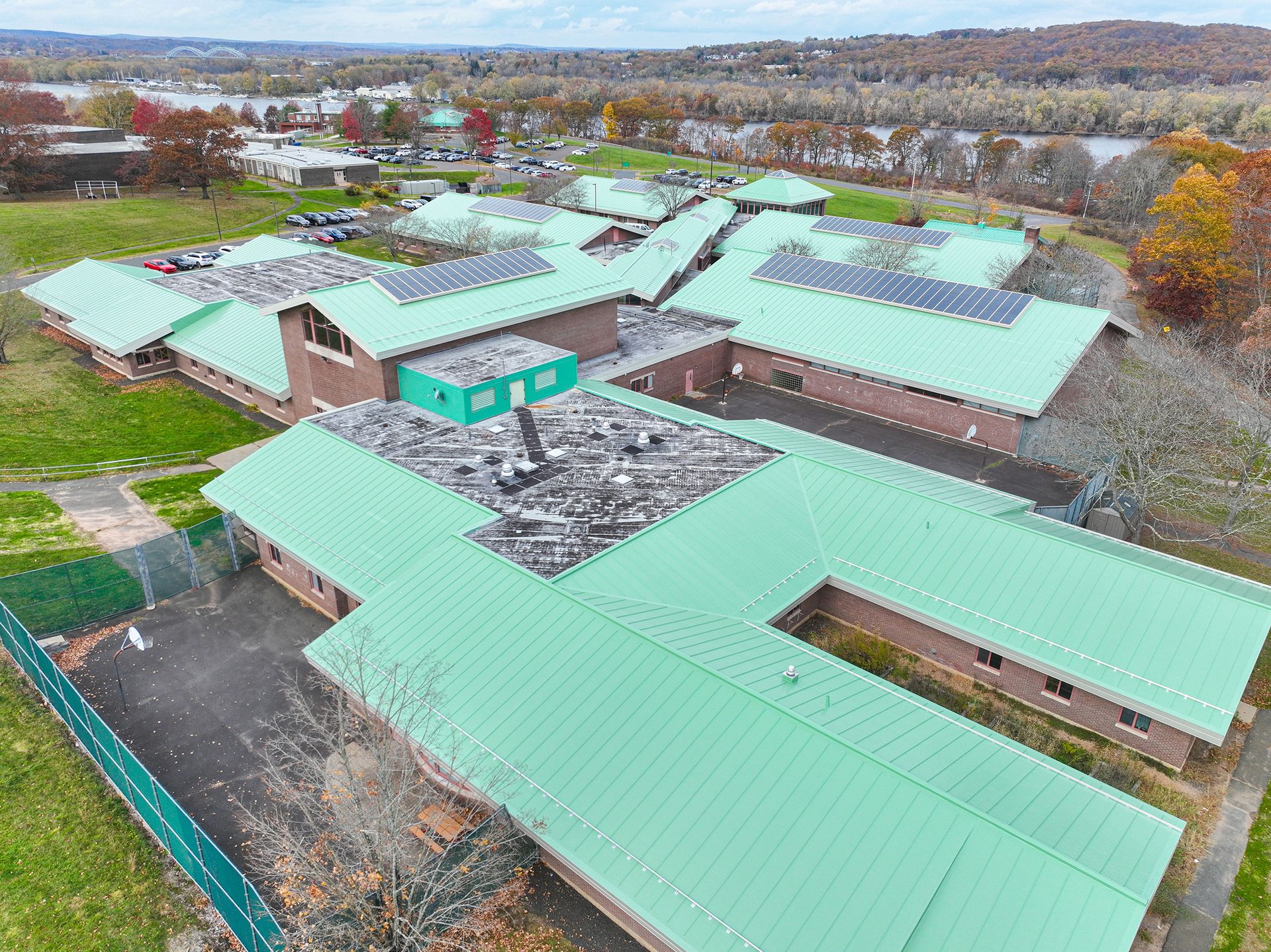 Aerial view of a school building with green roofs, solar panels, a river, and autumn trees.