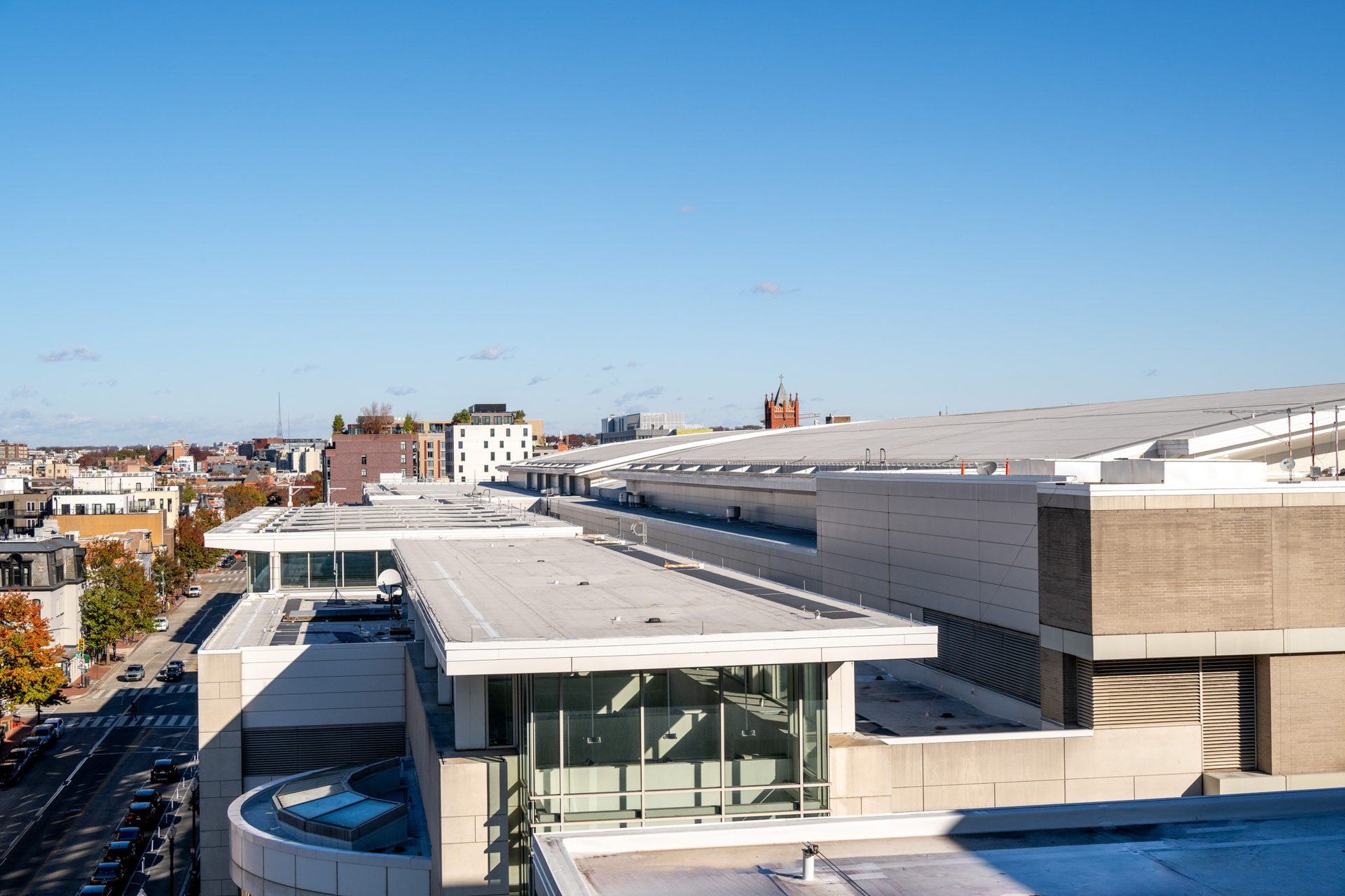 Aerial view of modern building rooftops in a city, with a distant skyline, street, and blue sky.