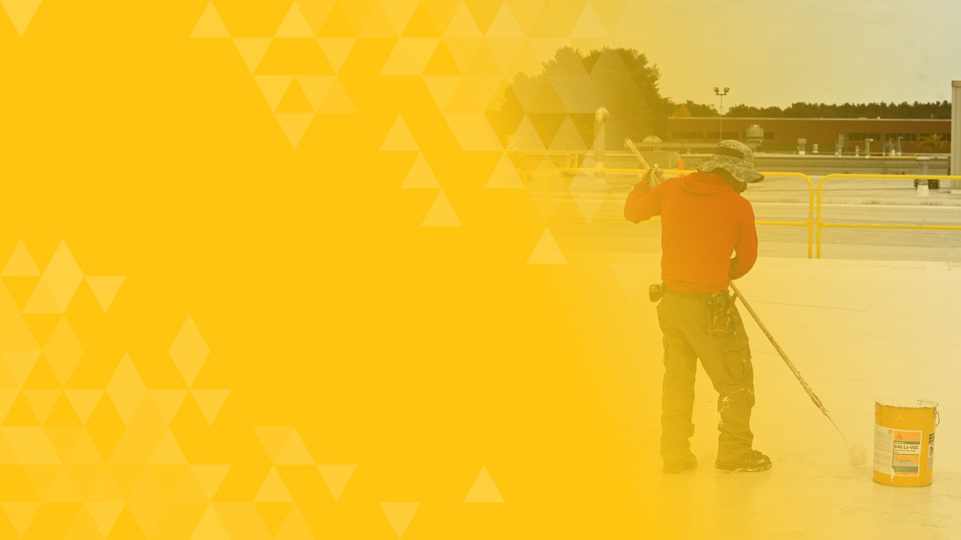 Worker in red shirt and hat uses a roller to apply a coating to a large surface, yellow bucket nearby.