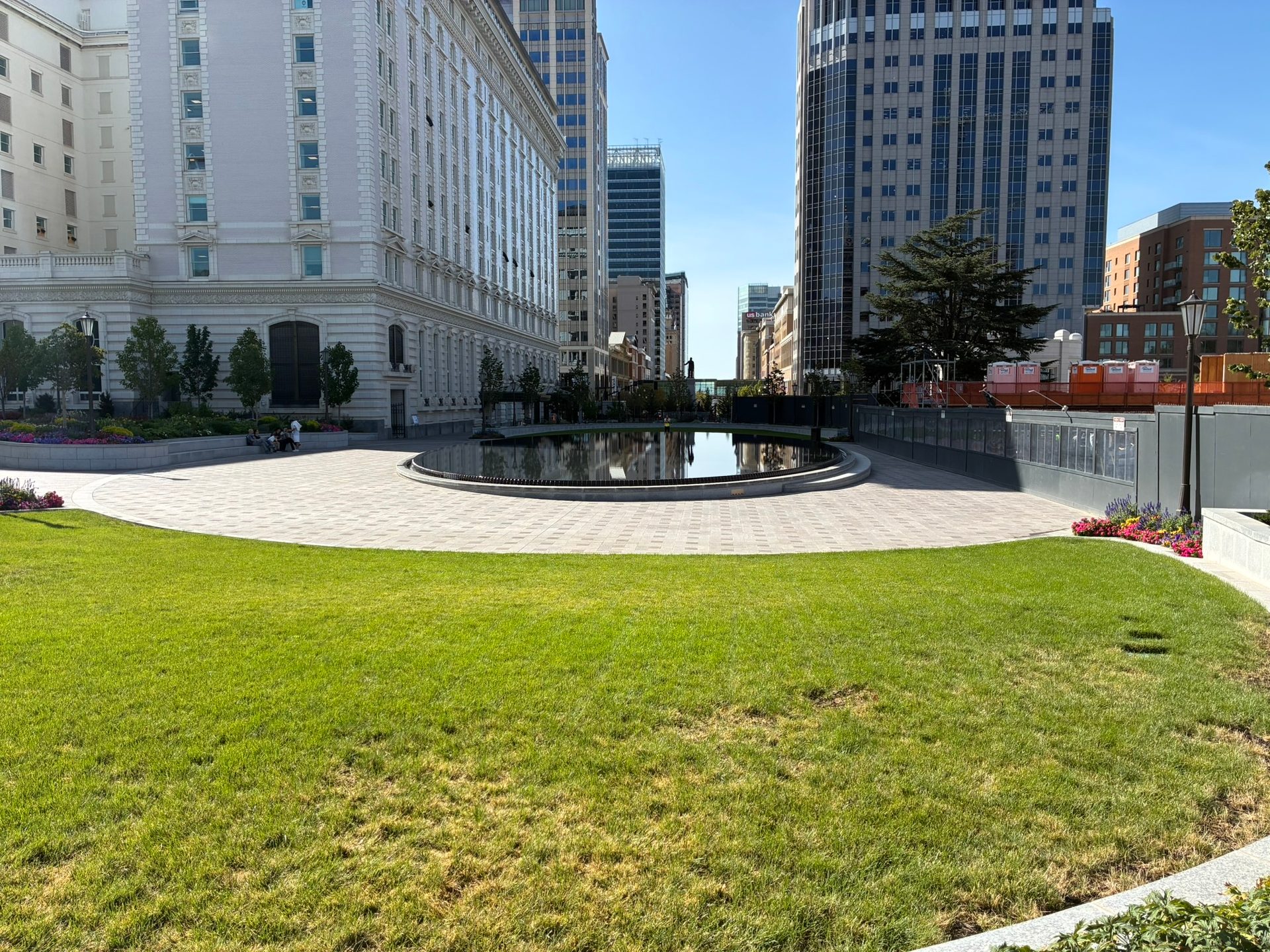 A vibrant urban park featuring a reflecting pool, flanked by a classical white building and a modern skyscraper.