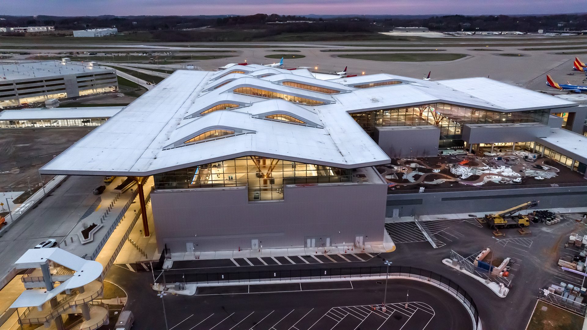 Modern airport terminal with distinctive white roof and curved skylights, airport grounds visible.