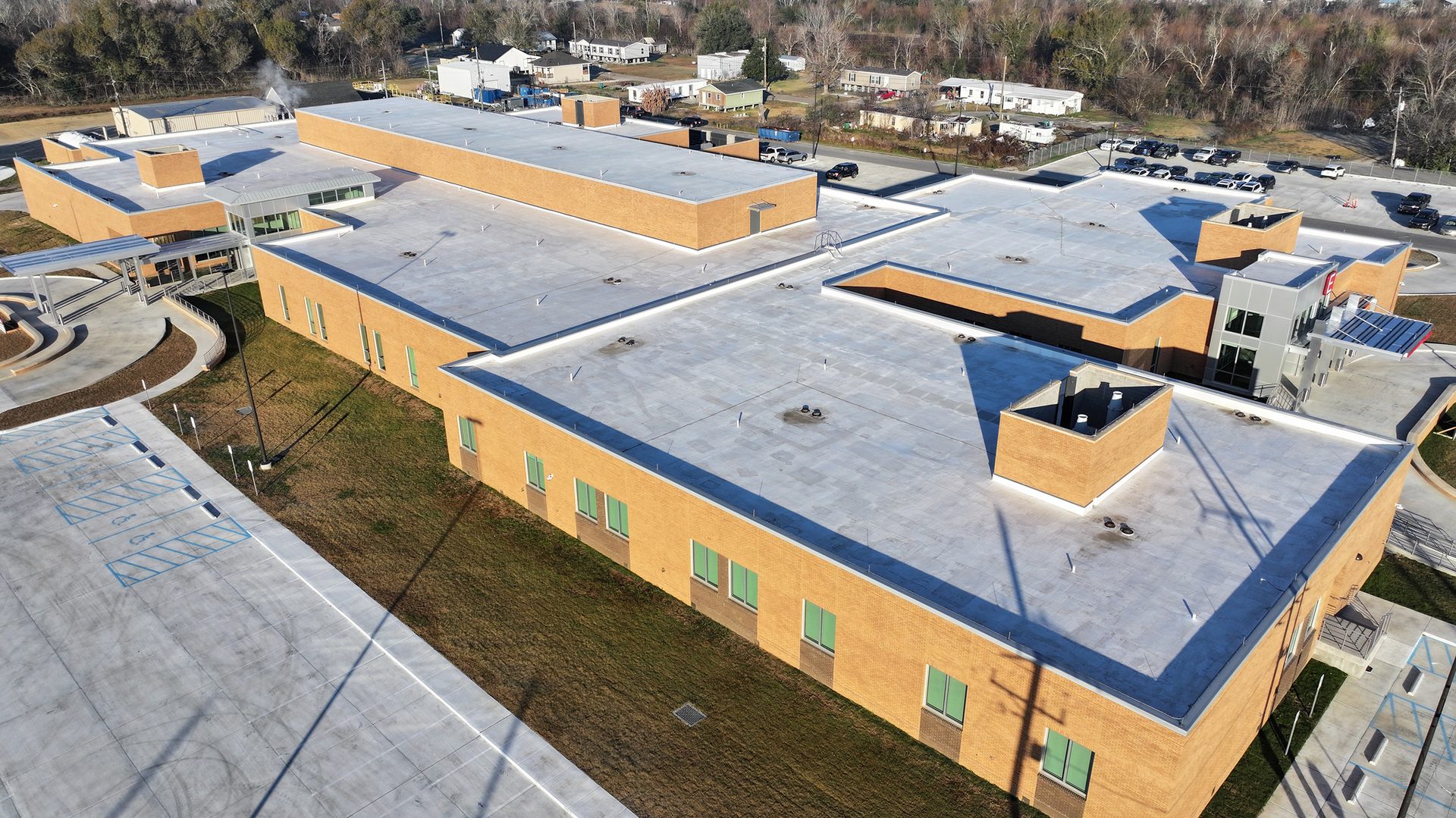 Aerial view of a modern school building with a flat roof, brick walls, and a large parking lot.