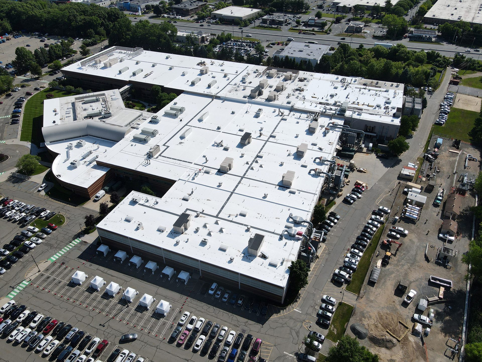 Aerial view of a sprawling white-roofed building complex with multiple parking lots and white tents.