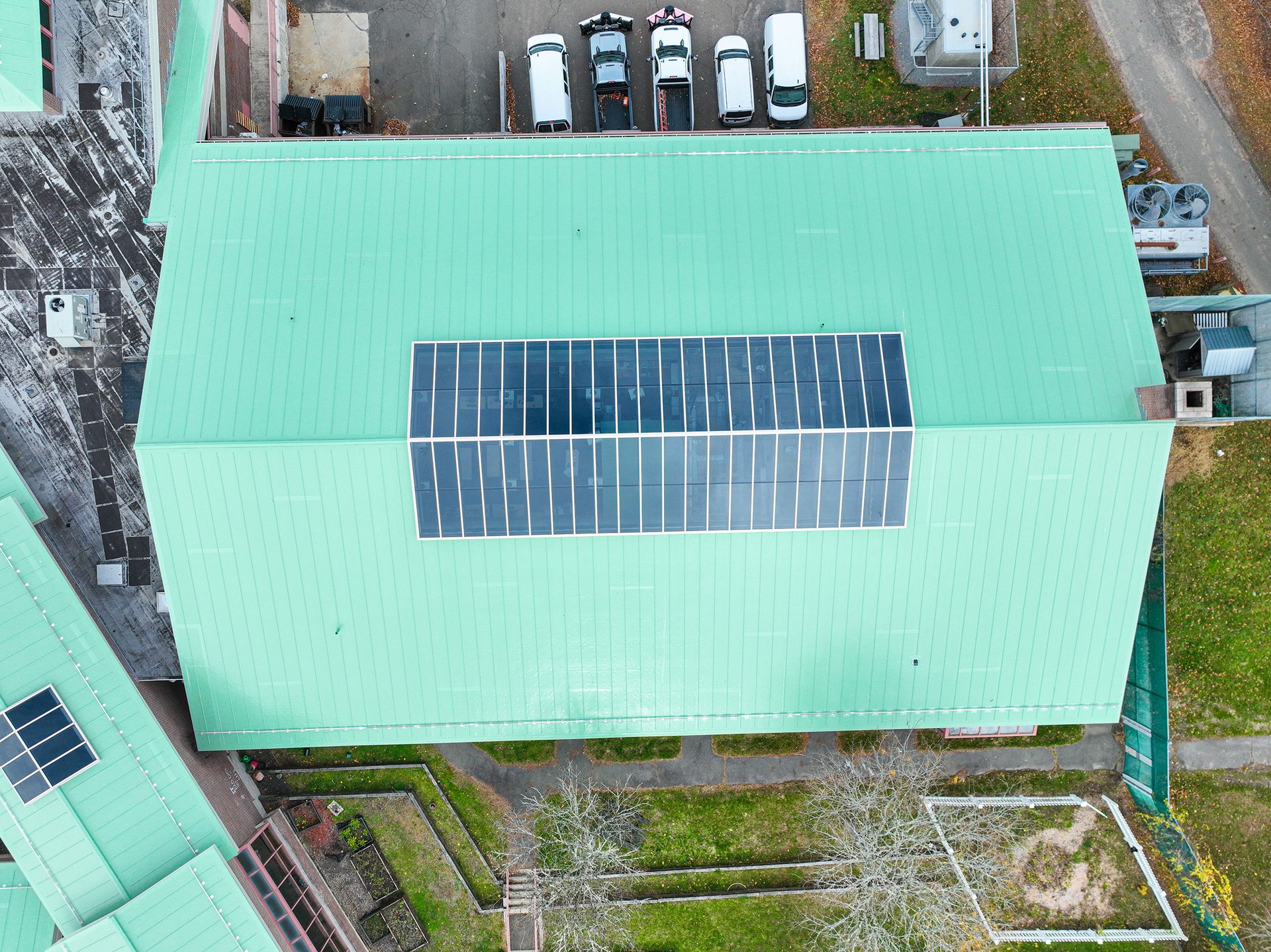 Aerial view of a building with a green roof and large solar panels, surrounded by a parking lot and green space.