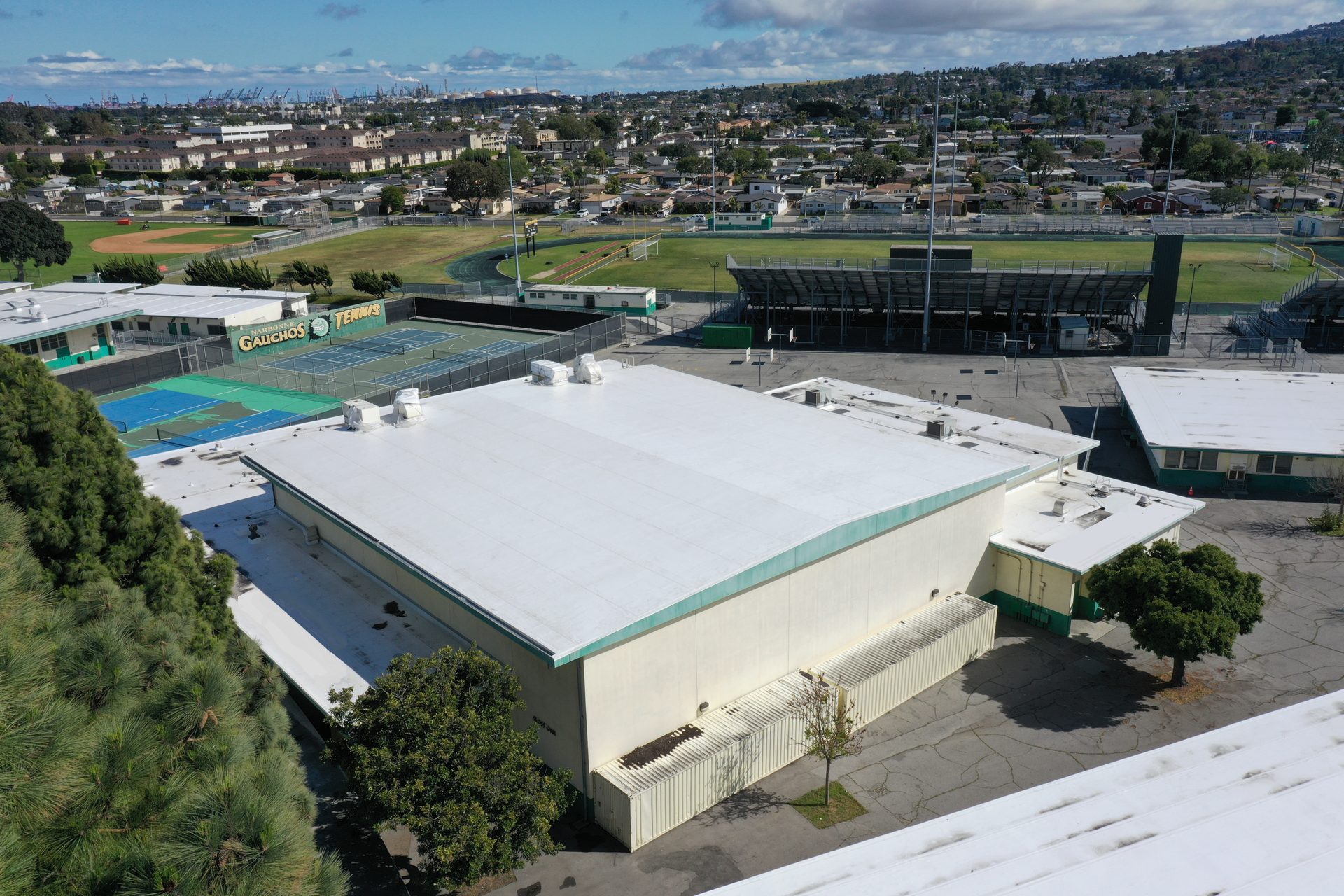 Aerial view of a school campus with a large building, tennis courts, and a sports complex.