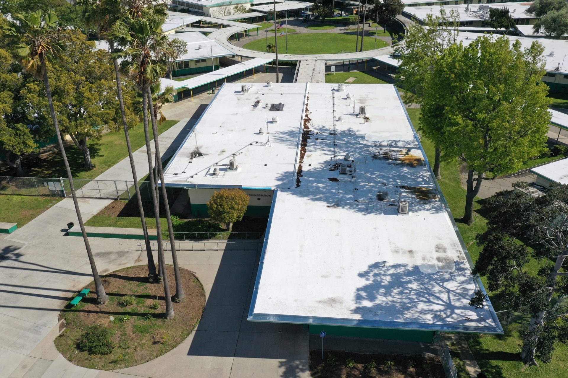 Aerial view of a school campus featuring white-roofed buildings, palm trees, and circular structures.