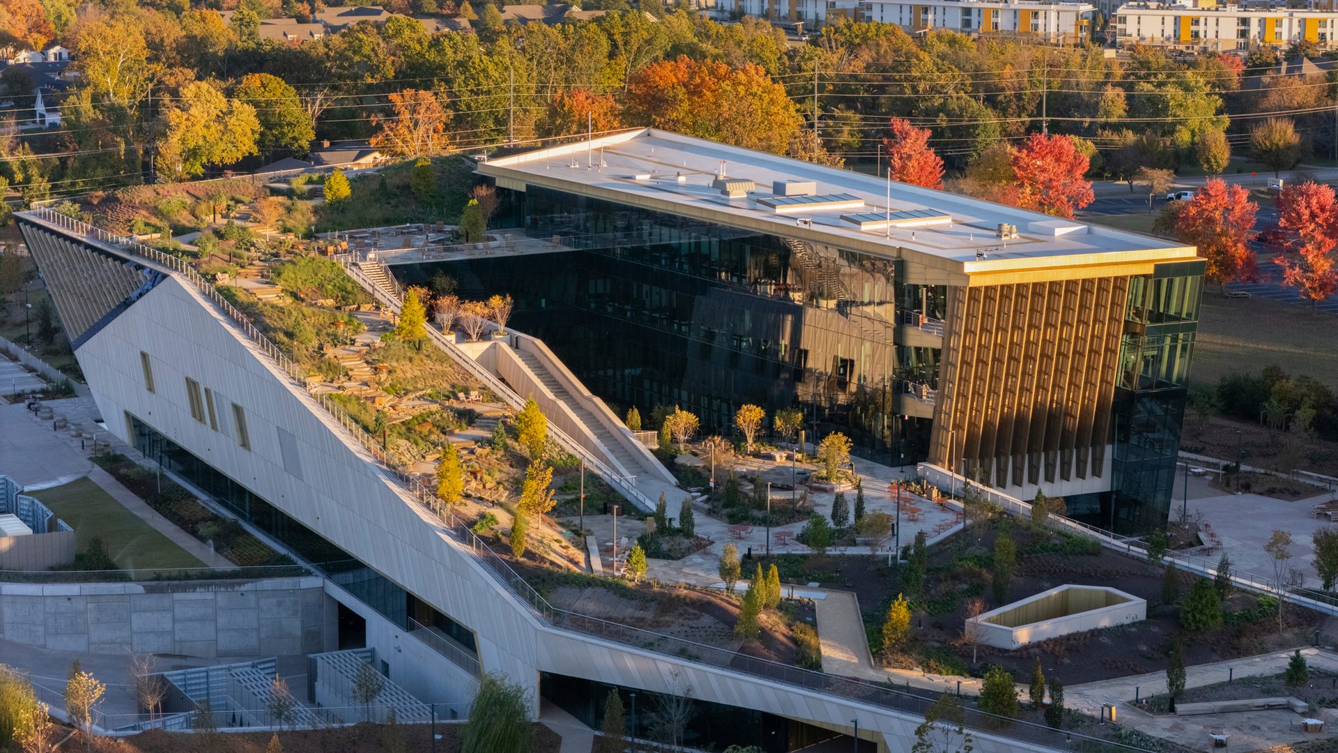 Aerial view of modern building complex with green roof gardens and glass office facade amidst autumn trees.