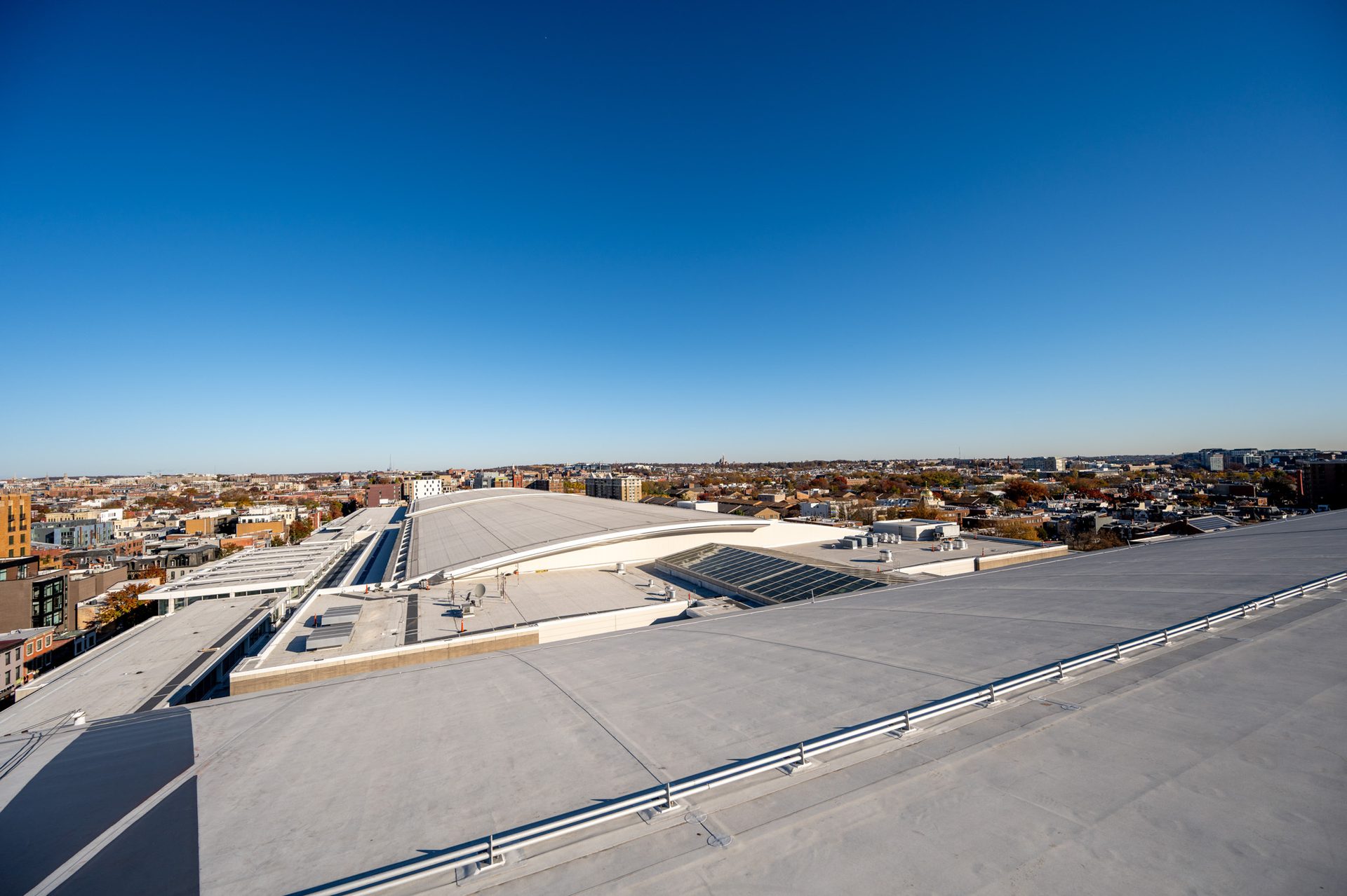 Aerial view of modern city rooftops and urban landscape under a clear blue sky on a bright day.
