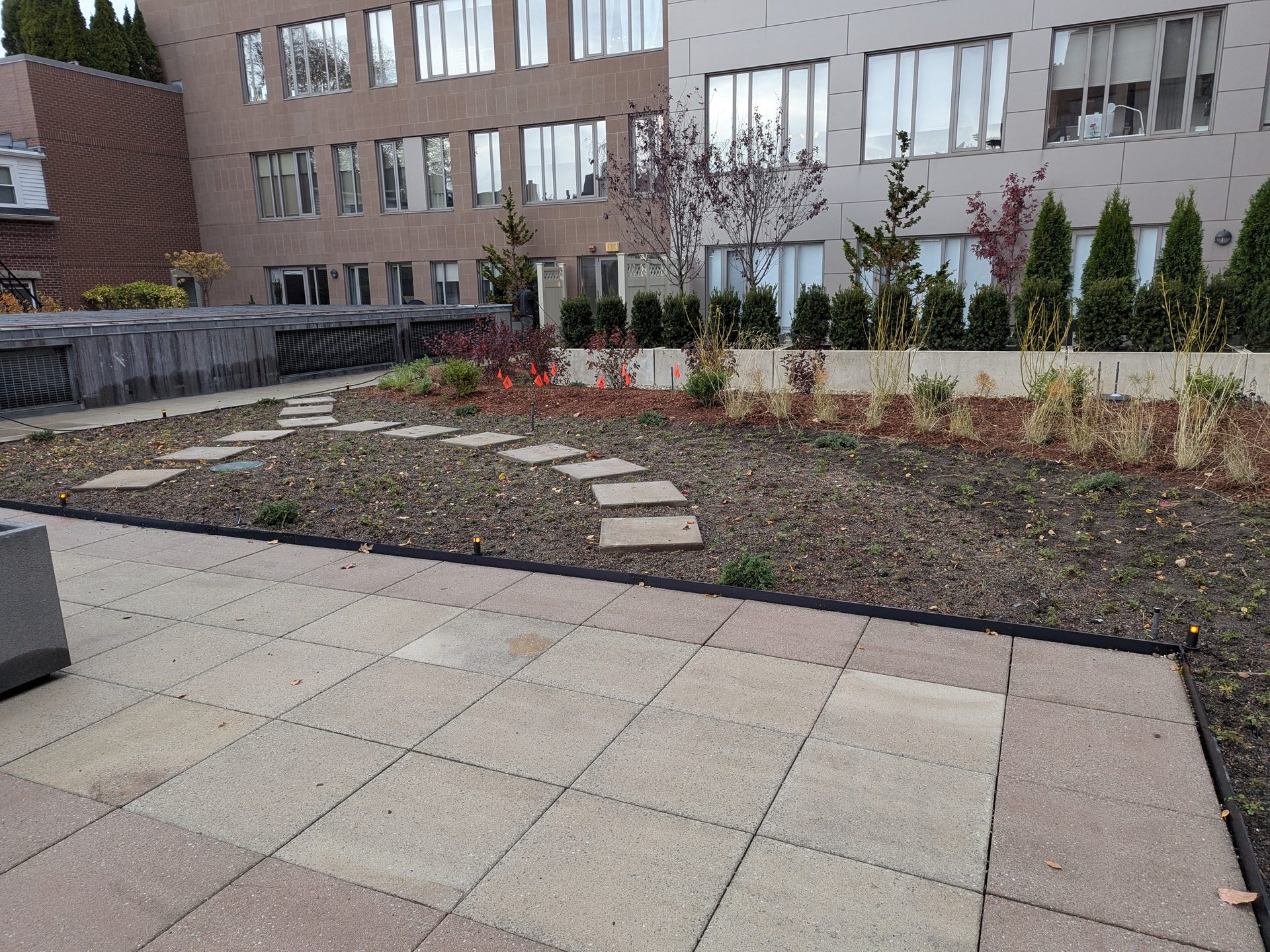 A rooftop patio area with paving stones, a garden bed with a curved stepping stone path, and buildings.