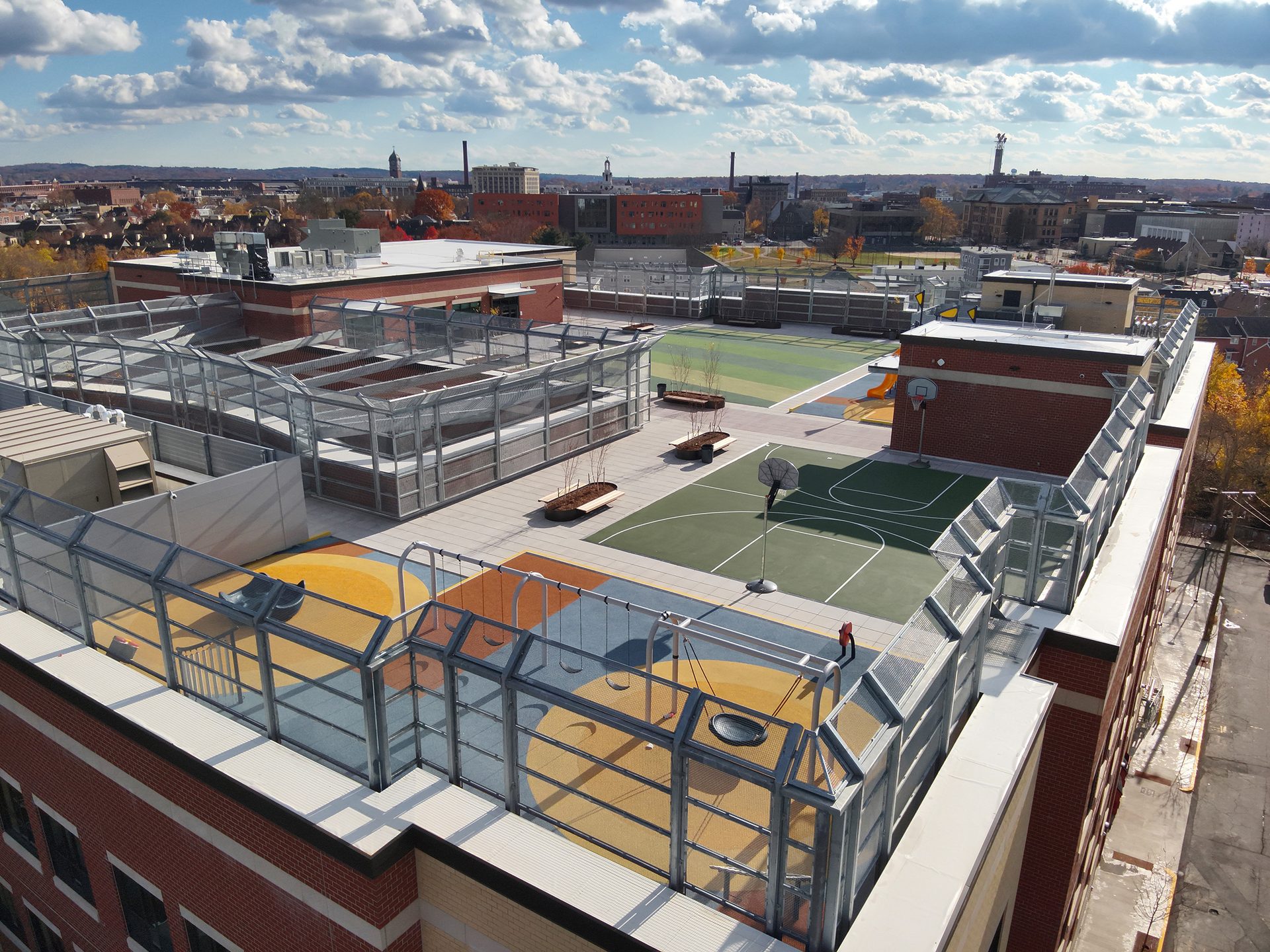 Aerial view of a vibrant urban rooftop featuring a playground, basketball court, and garden beds.