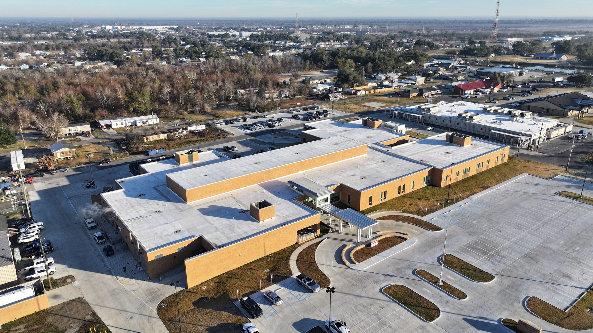 An aerial view reveals a sprawling modern L-shaped school building, surrounded by parking lots, with a distant town.