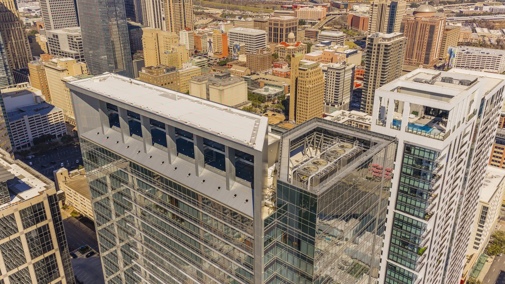 Aerial view of a dense city skyline with two modern high-rise buildings in the foreground, one with a rooftop pool.