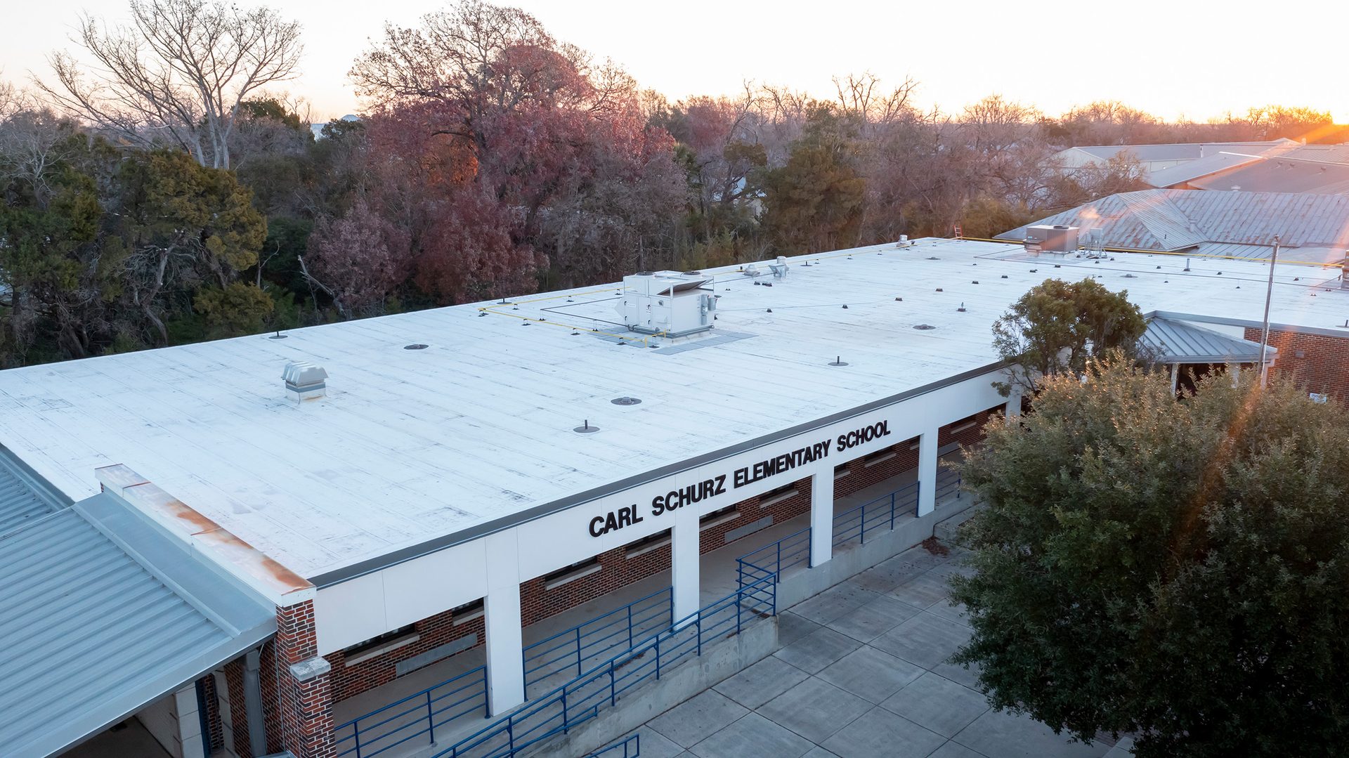 Aerial view of Carl Schurz Elementary School, showing its white roof, front entrance, and surrounding trees.