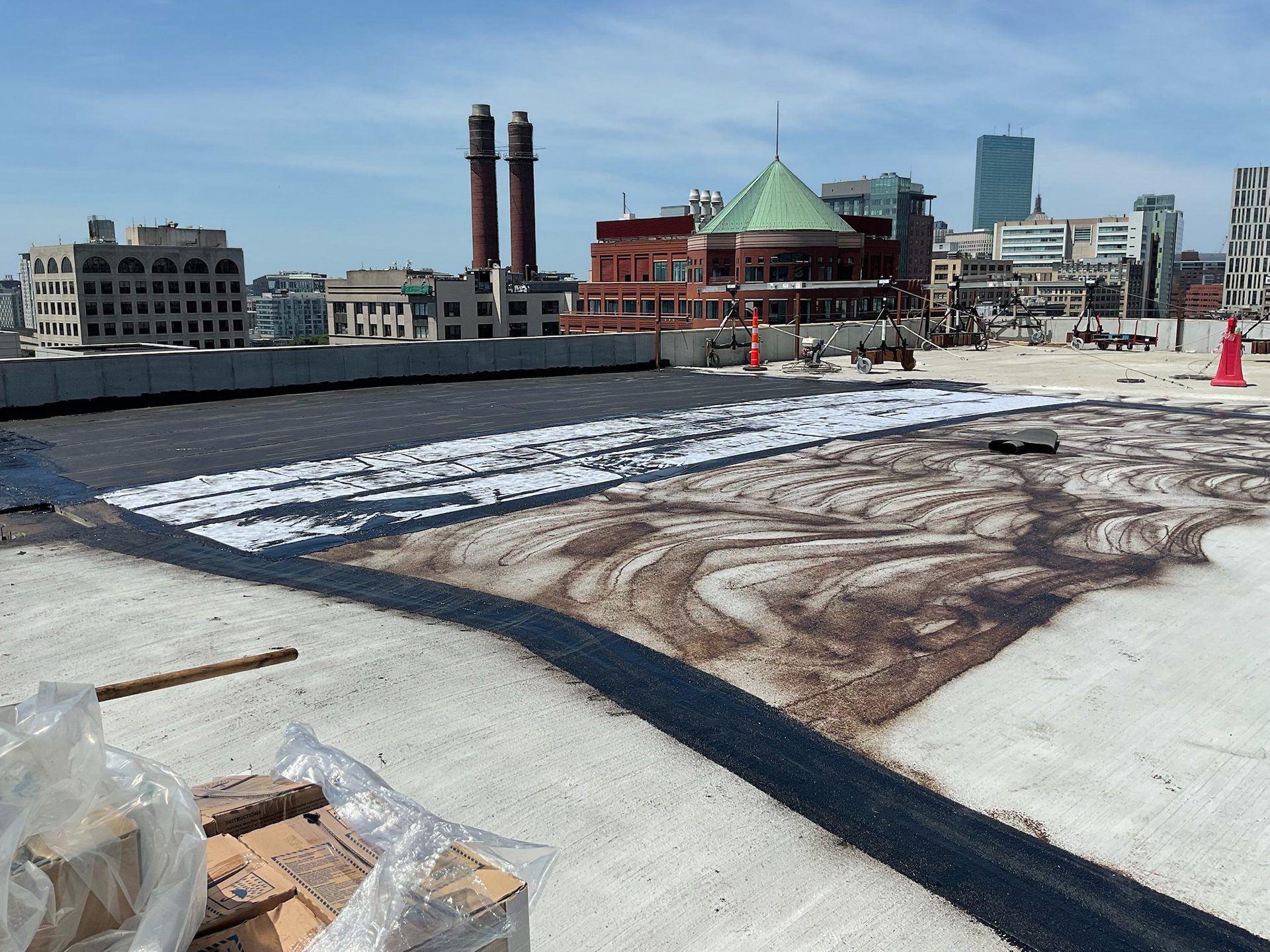 Rooftop renovation with black tar, white underlayment, and brown granules, against a city skyline.