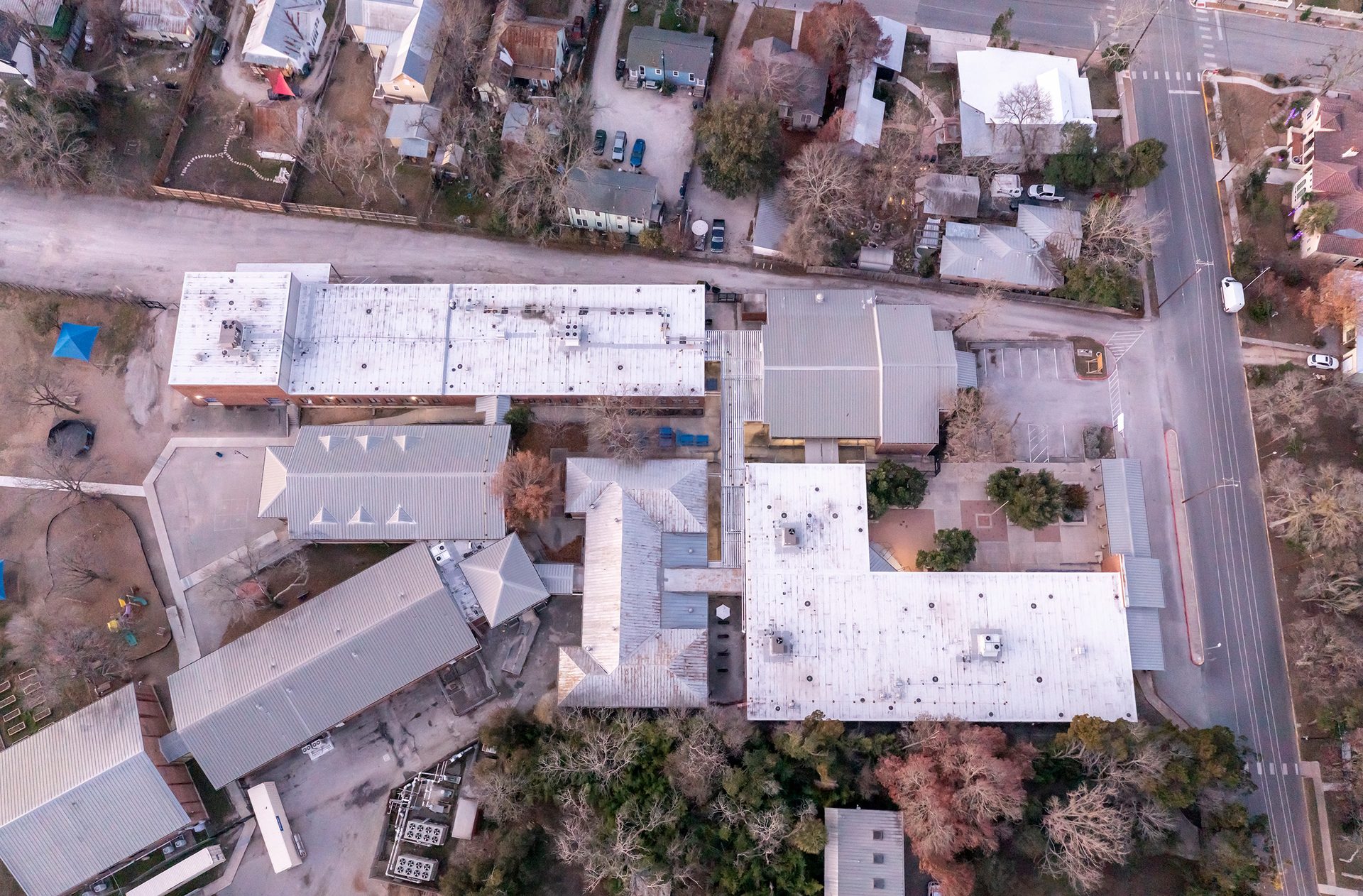 Aerial view of a building complex with light-colored roofs, surrounded by residential areas and roads.