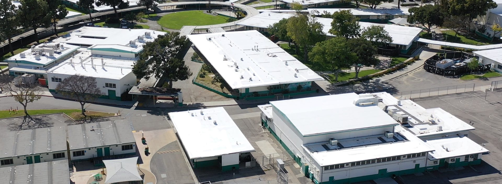 Aerial view of a school campus featuring numerous white-roofed buildings with green accents, interconnected by pathways.