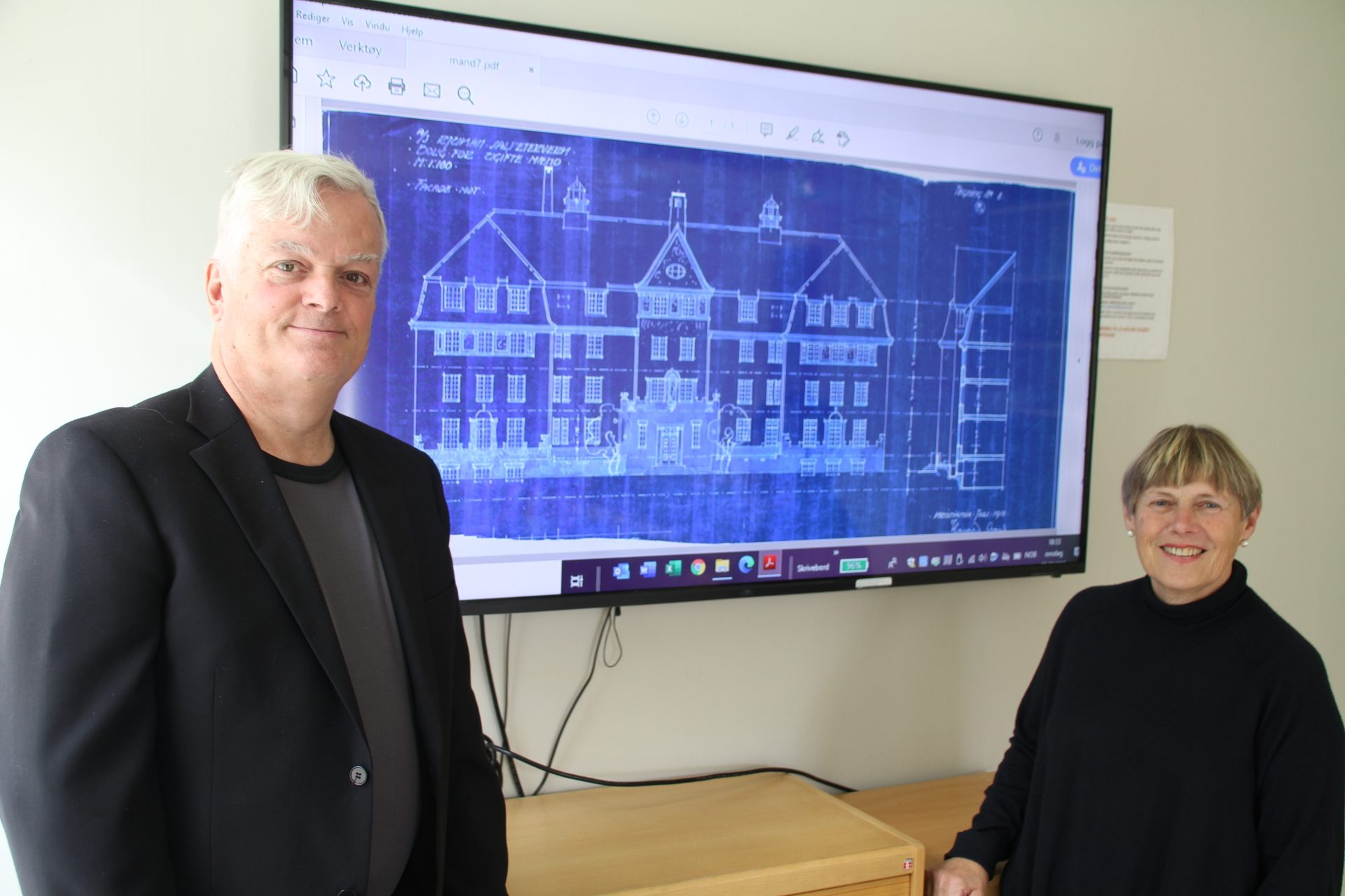 Man and woman in front of a large screen displaying a building blueprint.