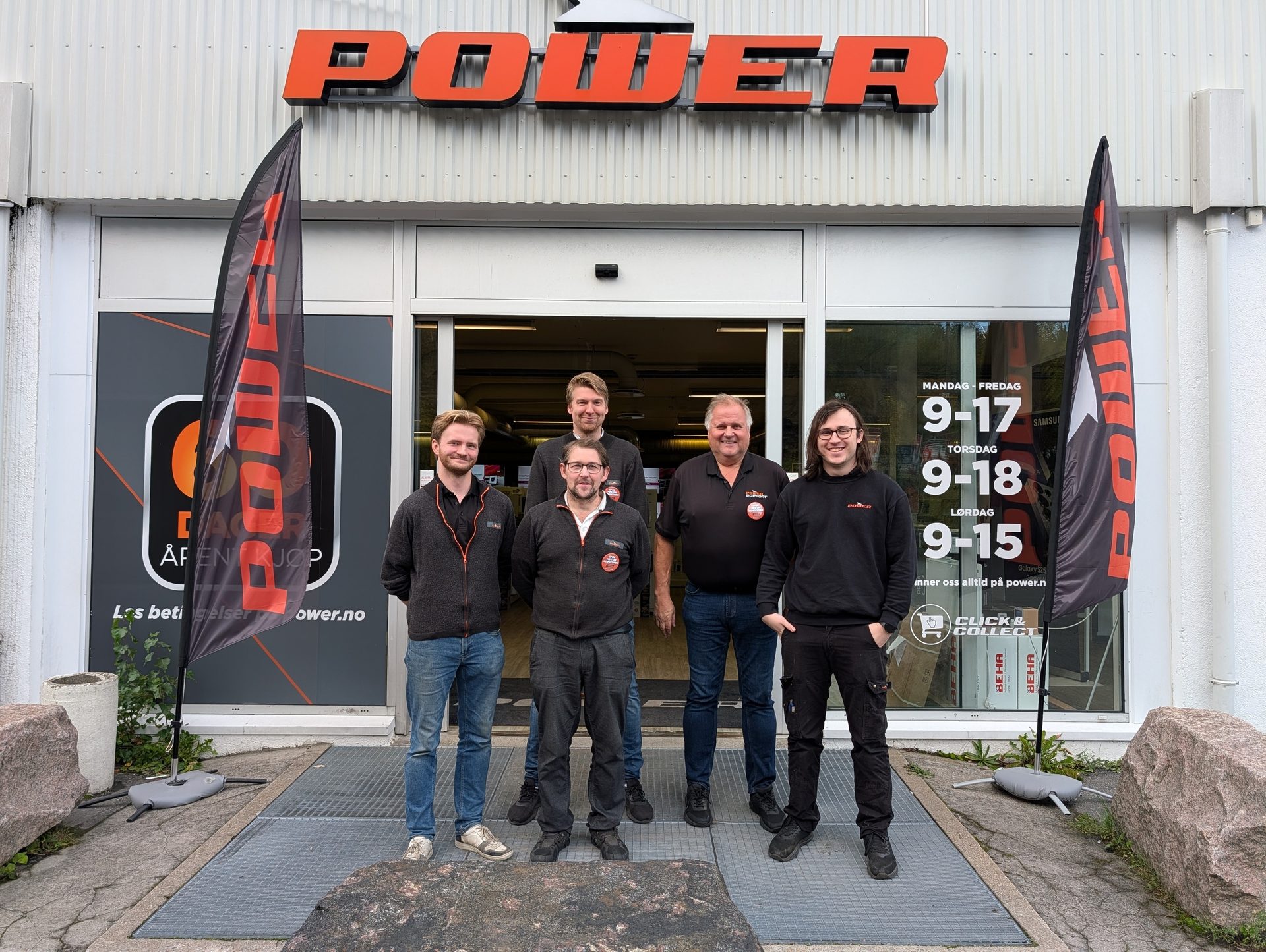 Five smiling male employees stand in front of a "POWER" electronics store.