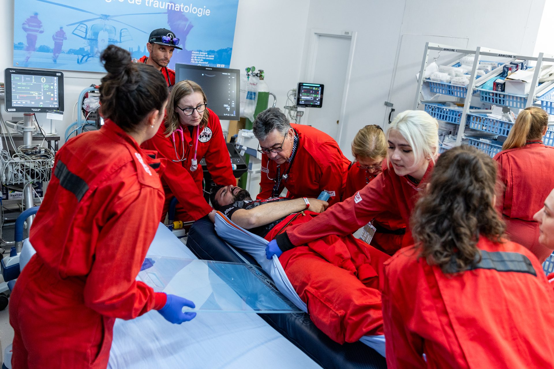A medical team in red jumpsuits attending to a patient on a stretcher in an emergency room setting.