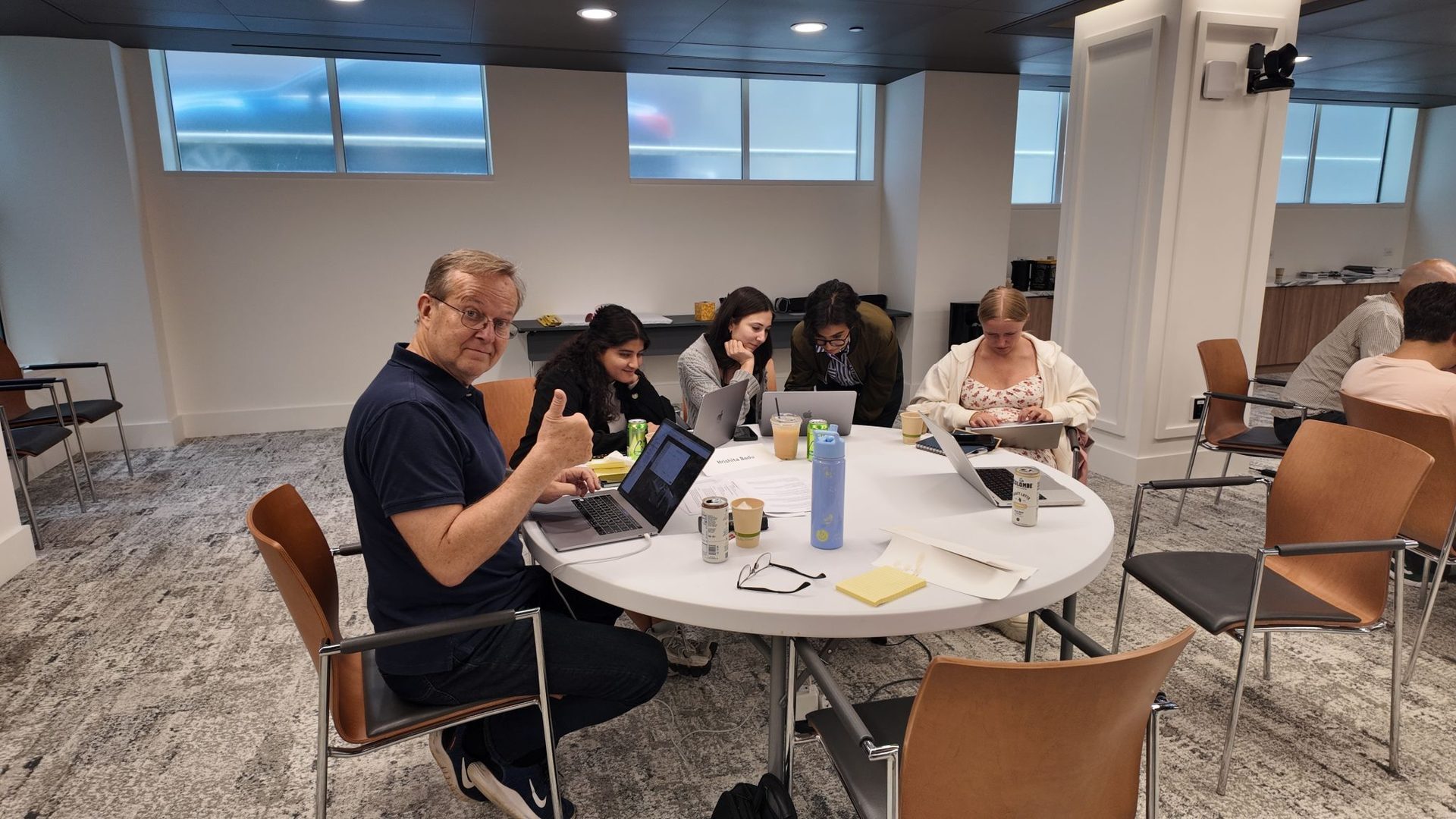 Group of people working on laptops at a table, one man gives a thumbs-up.
