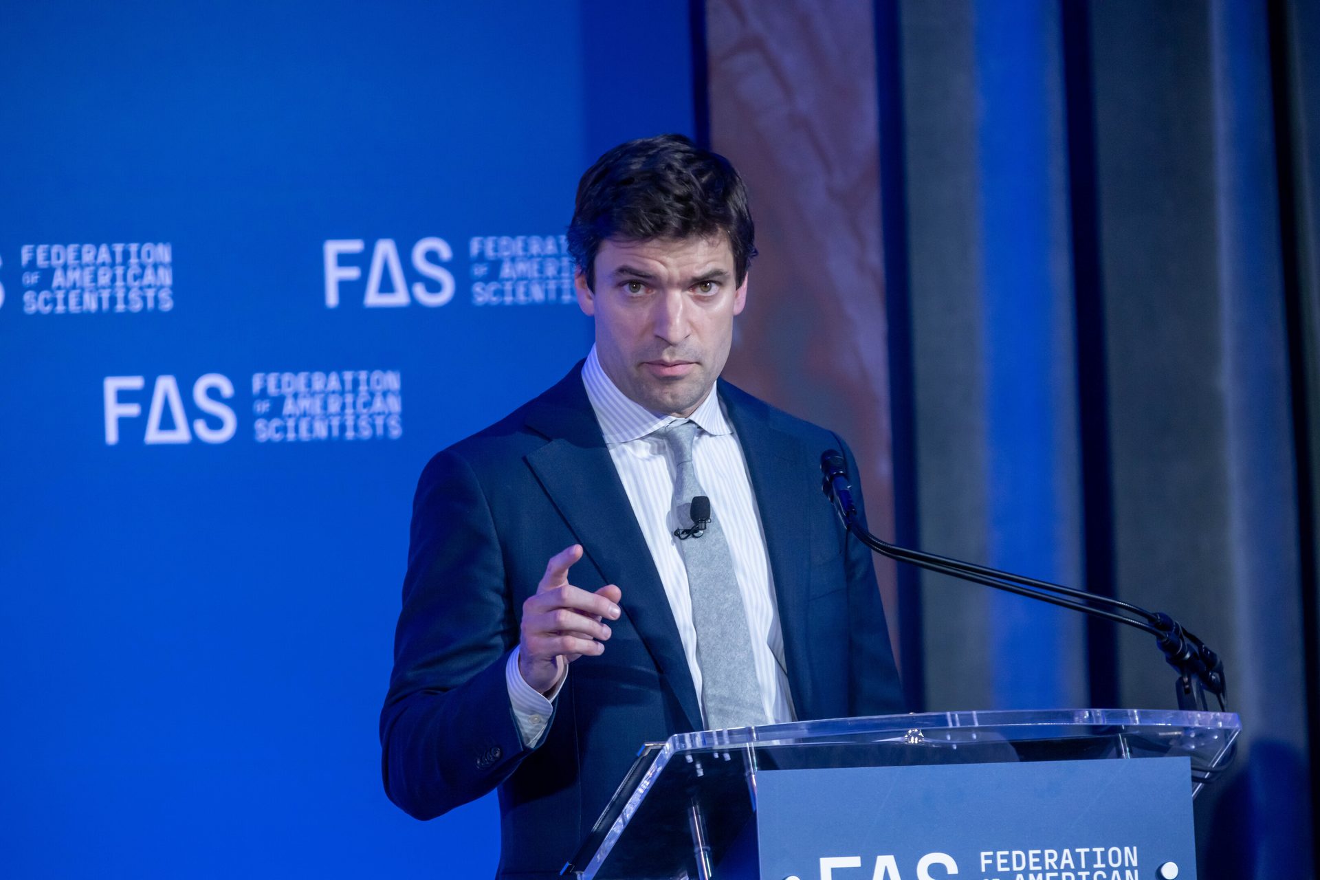 A man in a suit speaks at a podium with the Federation of American Scientists (FAS) logo in the background.