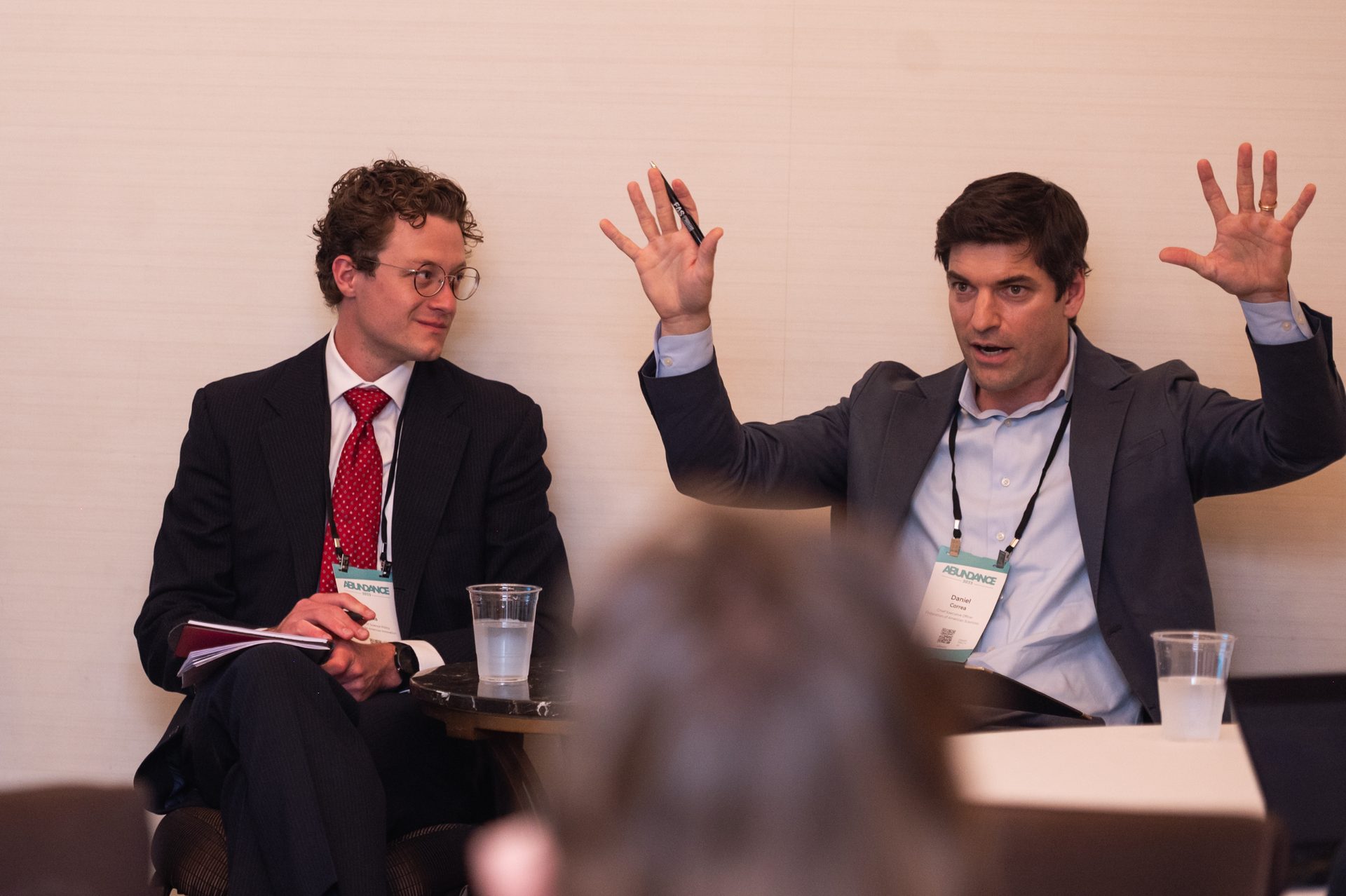 Two men, one speaking animatedly with hands raised, the other listening attentively.