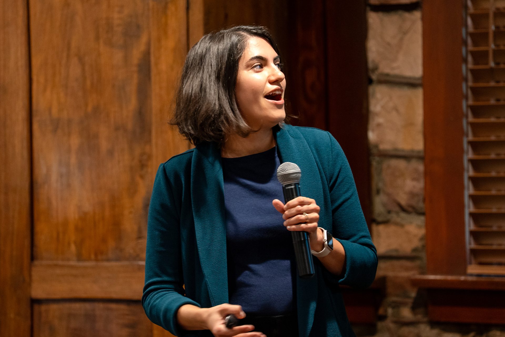 Woman in teal blazer speaking into a microphone.