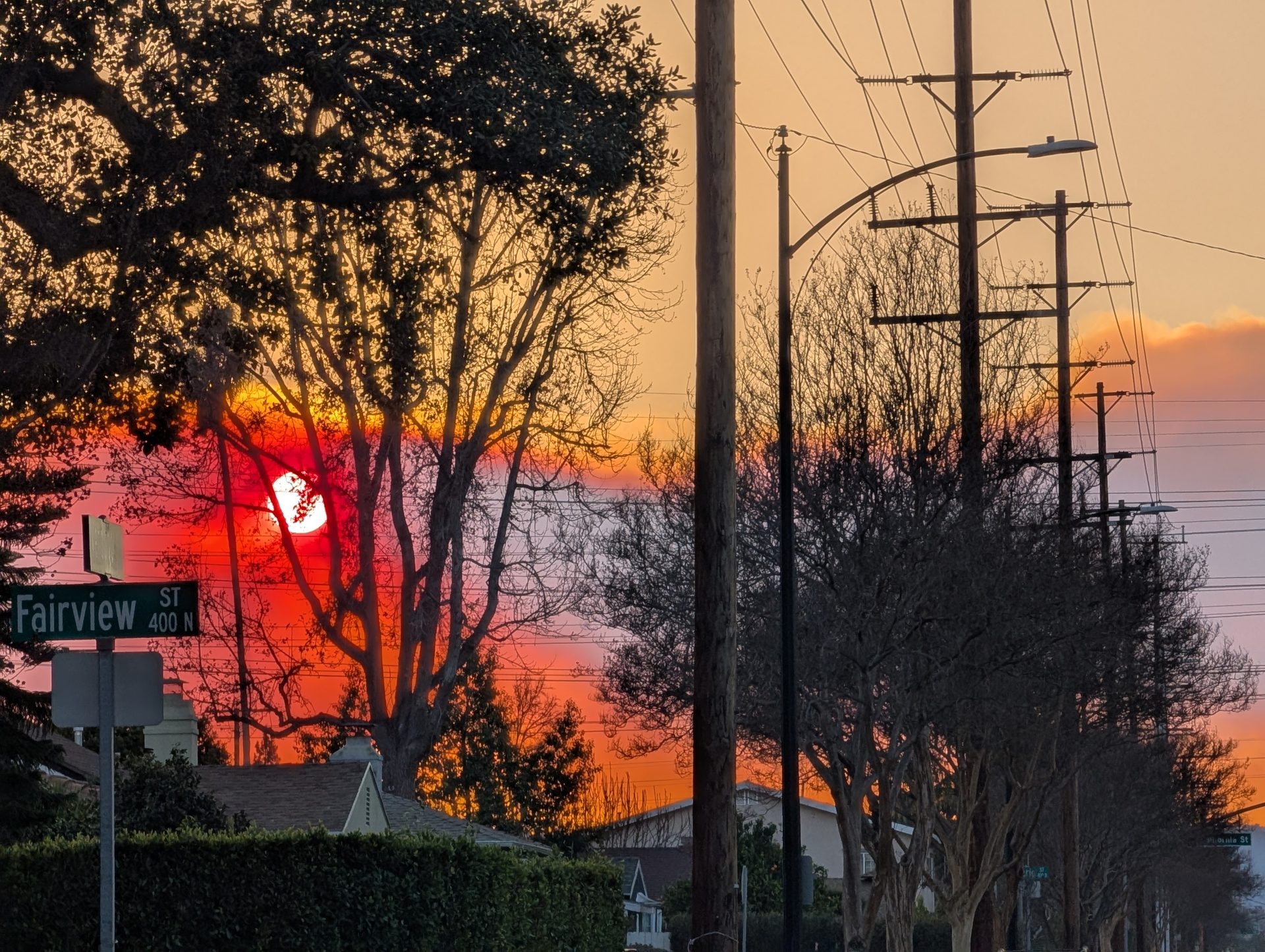 Red sunset through trees and power lines, with a Fairview Street sign.