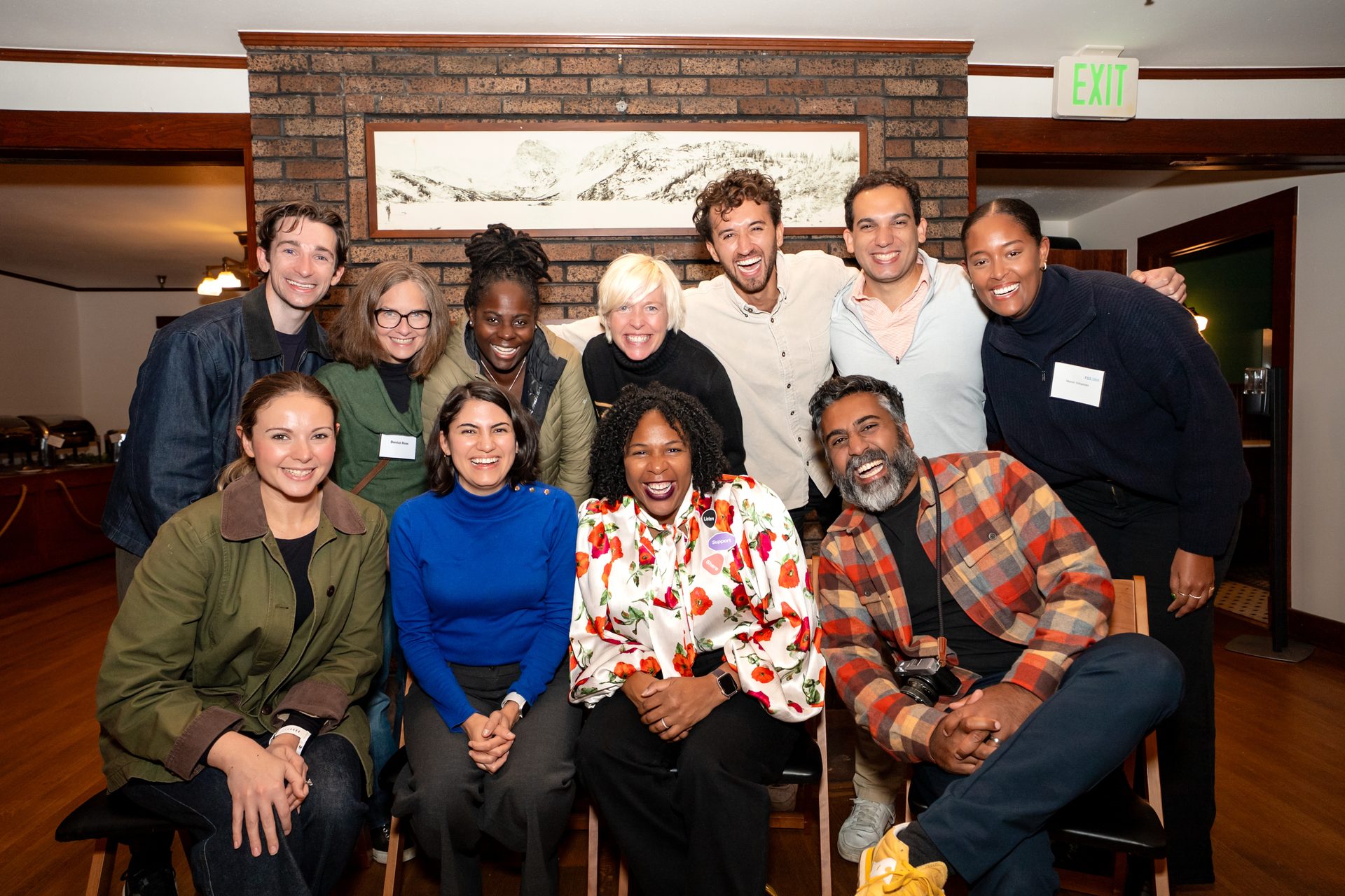 A diverse group of a dozen smiling people, some standing and some seated, posing for a group photo indoors.