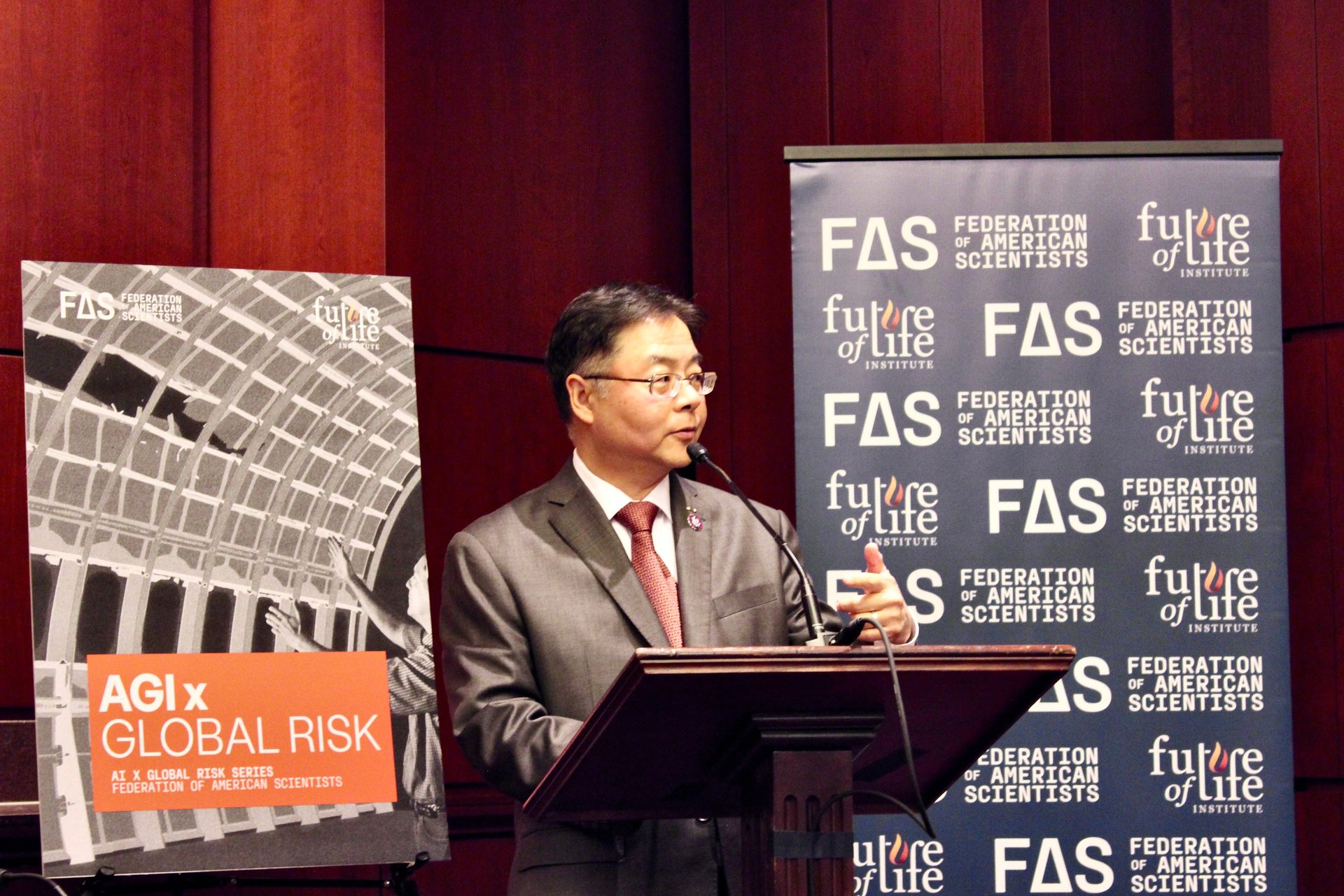 A man speaks at a podium, flanked by "AGI x GLOBAL RISK" and "FAS" / "Future of Life Institute" banners.