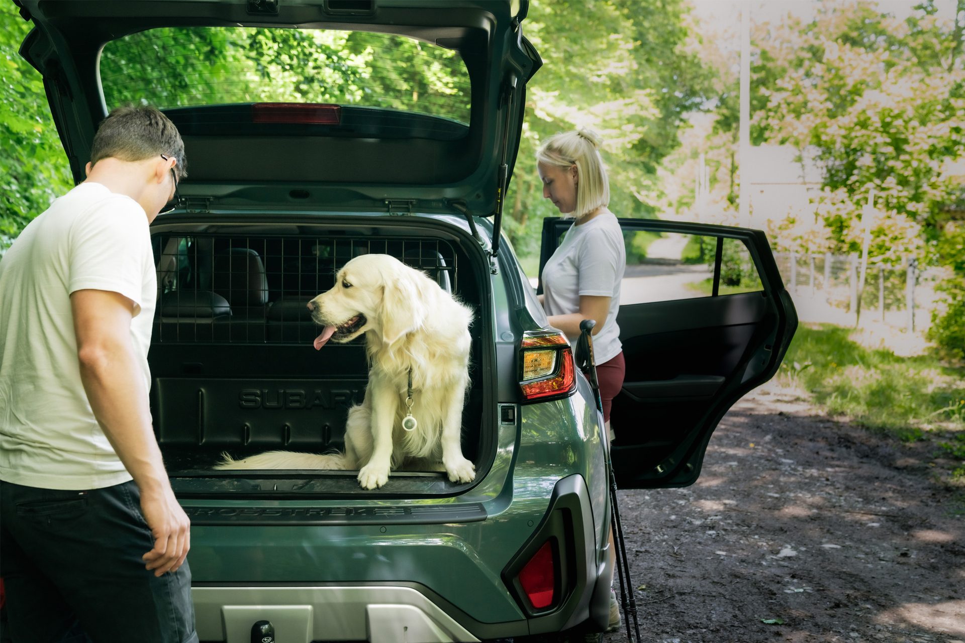 Golden retriever in Subaru Crosstrek trunk with two people outdoors.