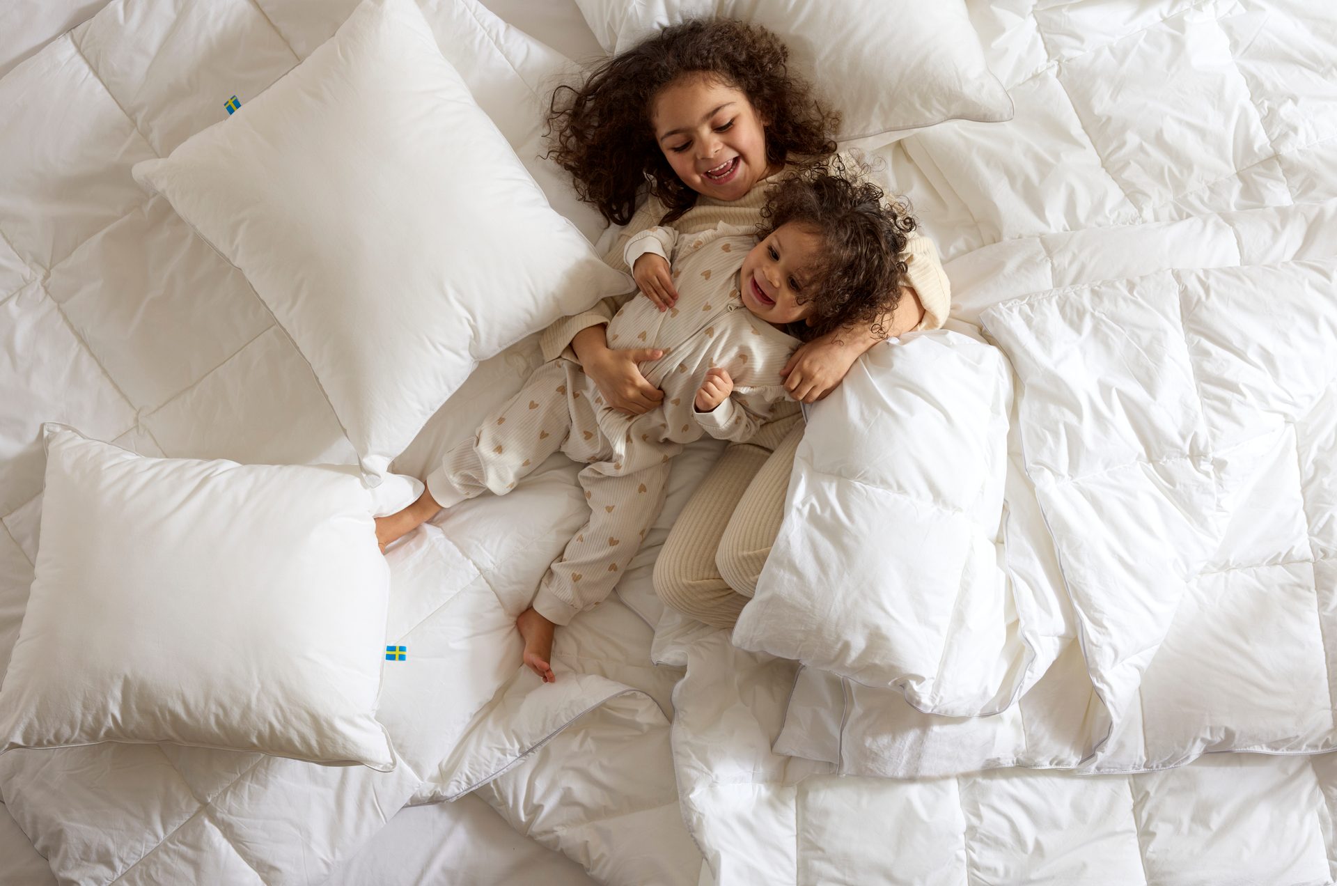 Happy kids hugging on white bed with Swedish flag tags.