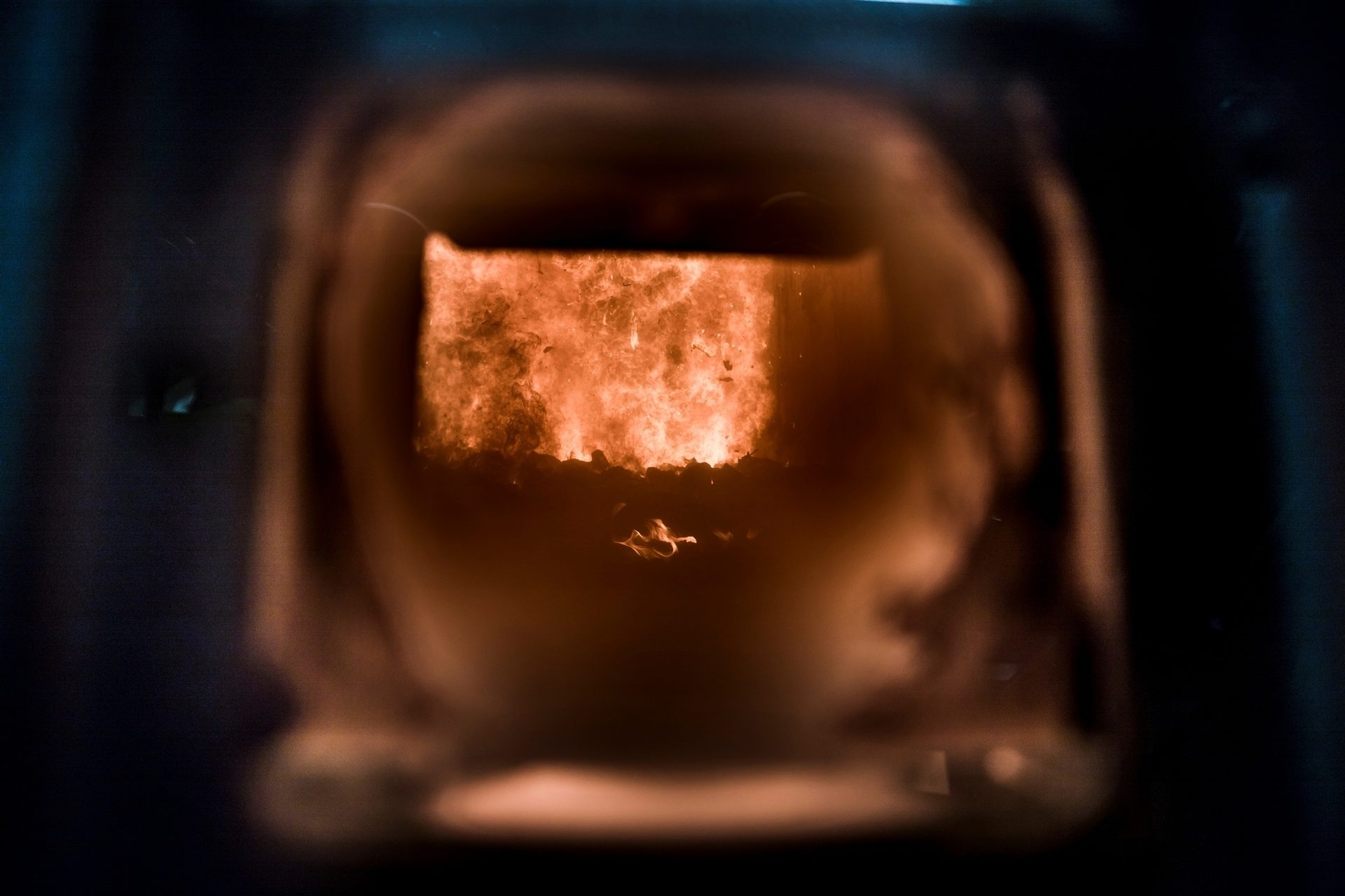 Intense orange and red flames blaze within a dark, blurry industrial furnace.