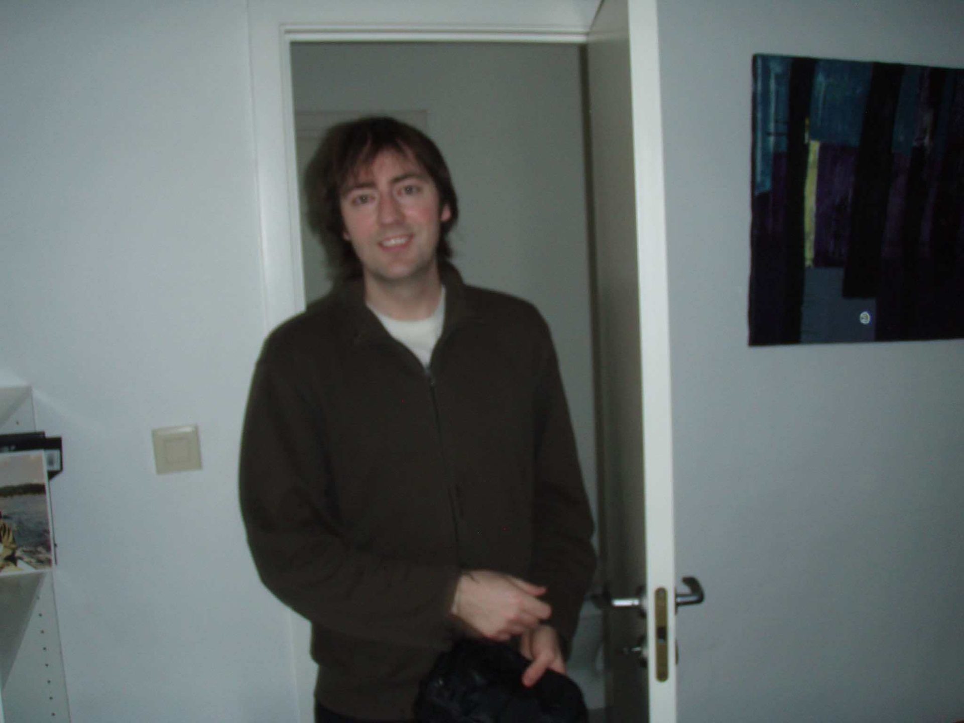Man in a dark jacket standing in a doorway, smiling at the camera.