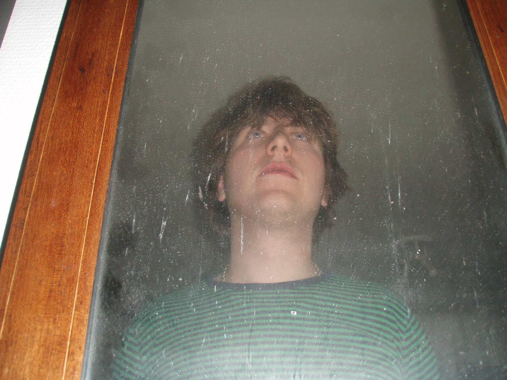 Reflection of a person with brown hair and striped shirt looking up in a dusty mirror.
