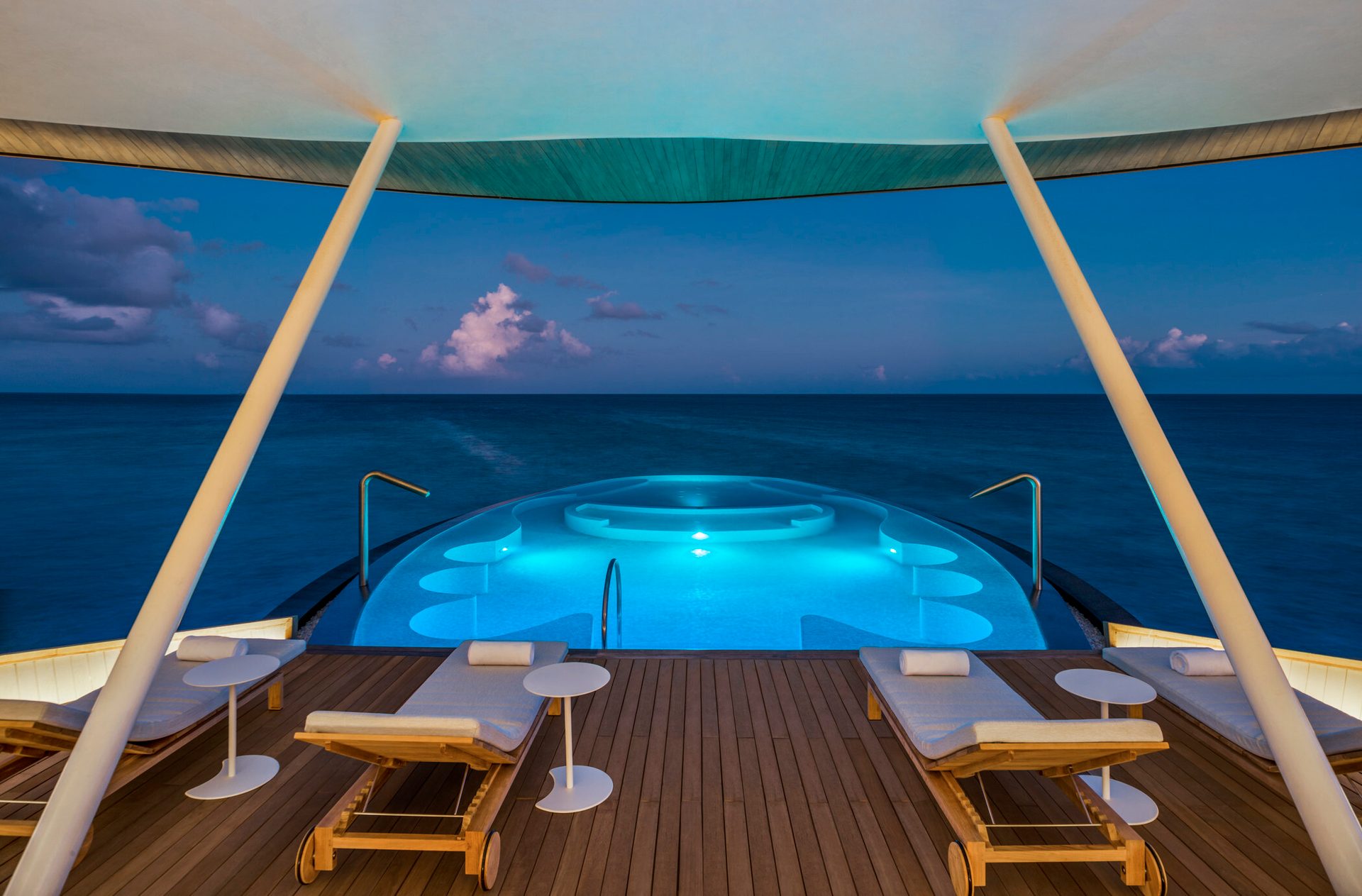 Overwater villa with blue-lit infinity pool, ocean vista, and lounge ...