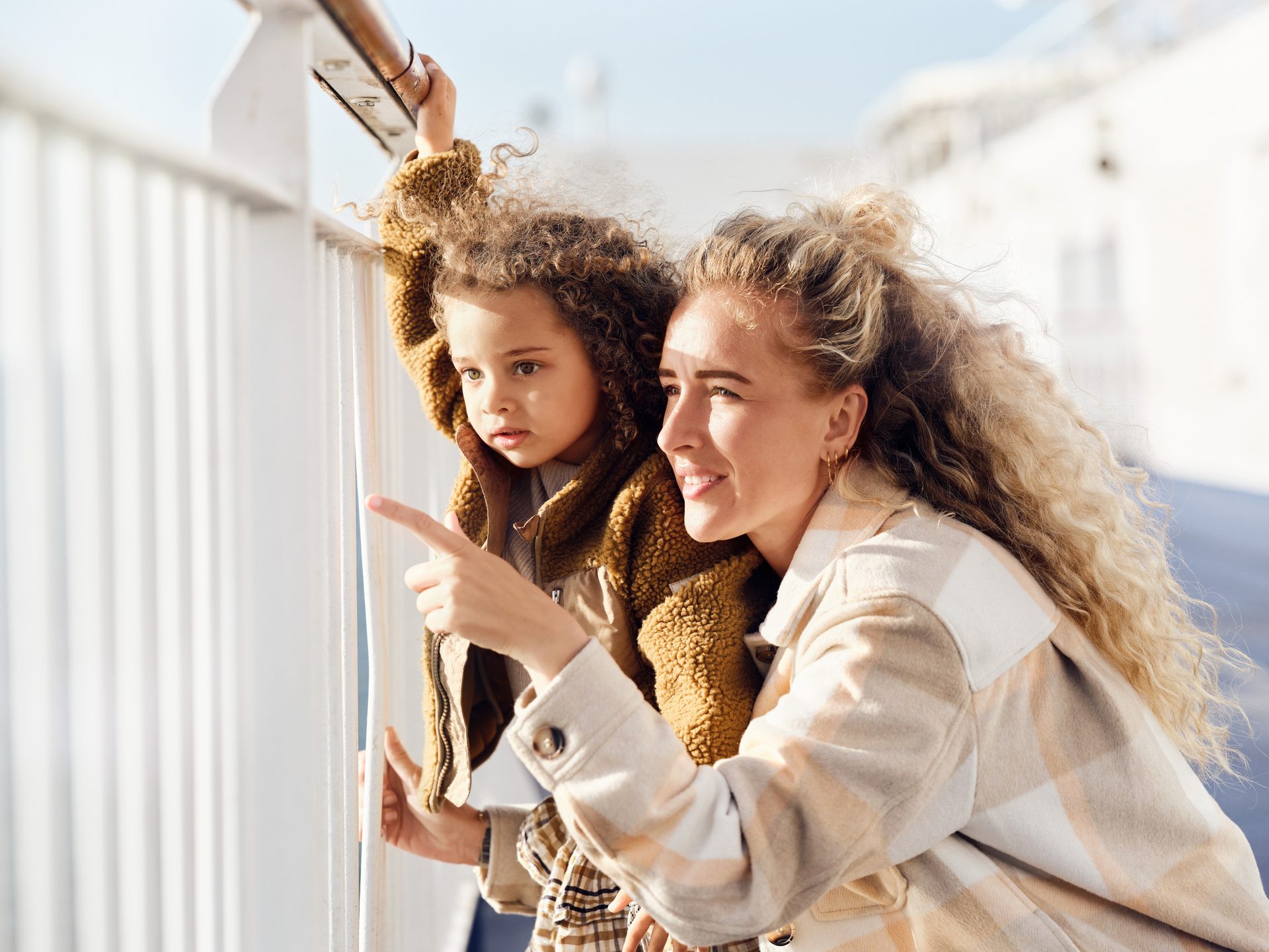 A mother and her young child look out from a boat railing, the mother pointing.