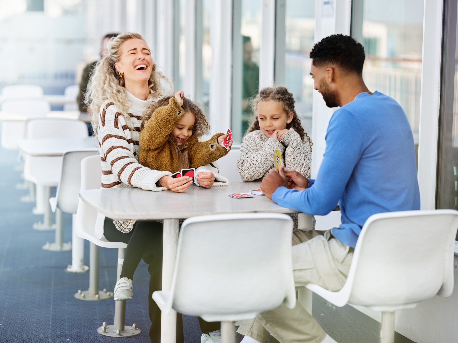 Family enjoying a card game on an outdoor deck, with a woman laughing and children playing cards.