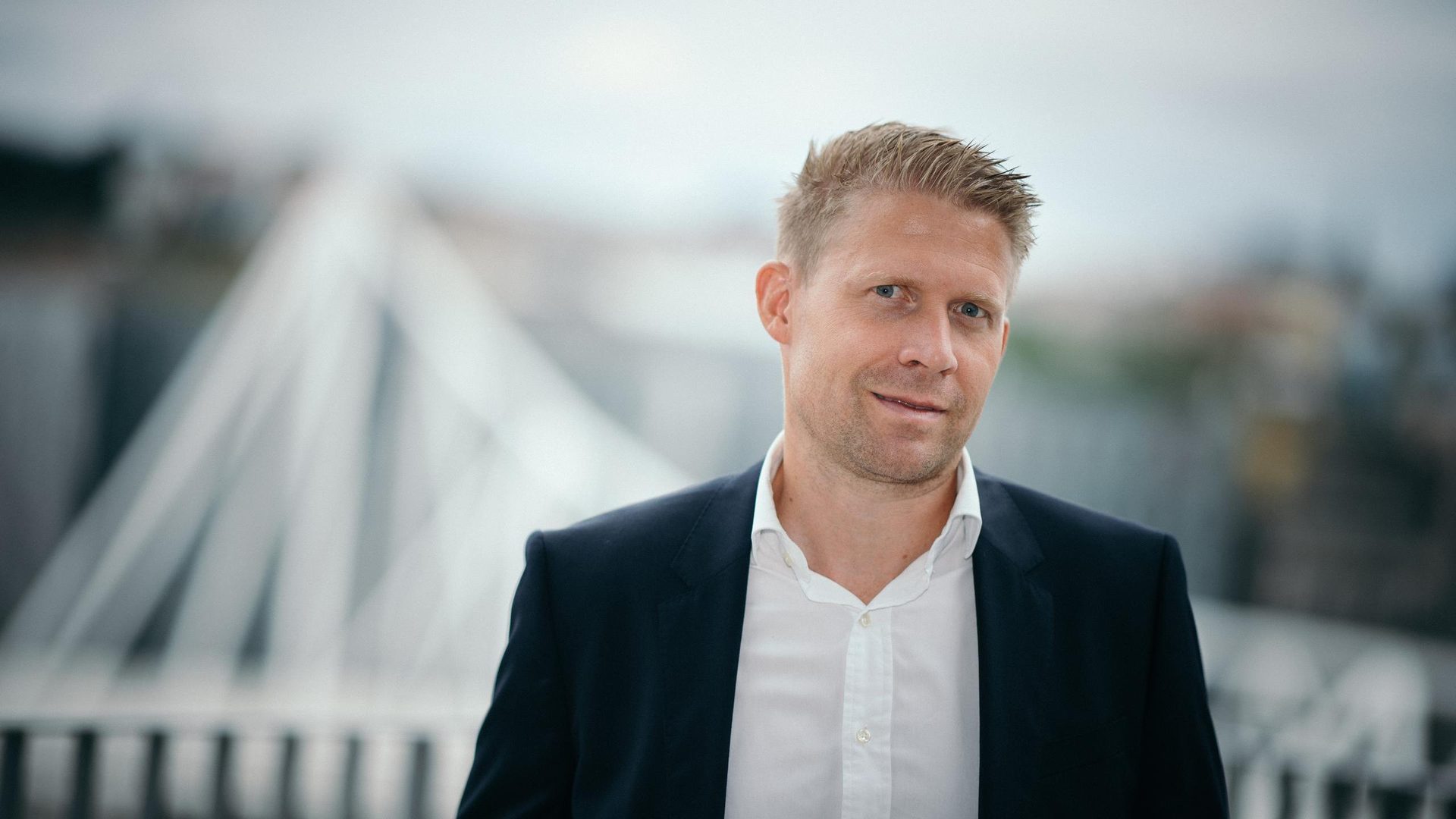 Headshot of a smiling blonde man in a dark suit with a blurred background.
