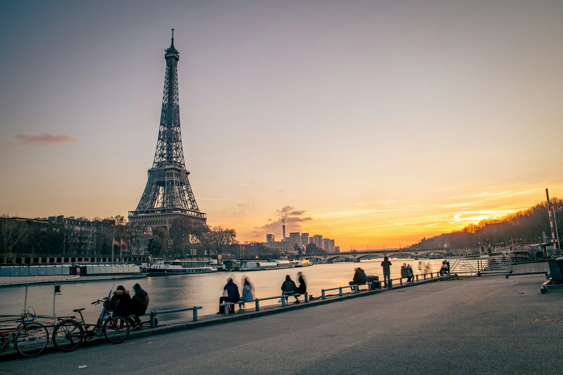 Paris sunset with Eiffel Tower, Seine River, and people relaxing by the water.